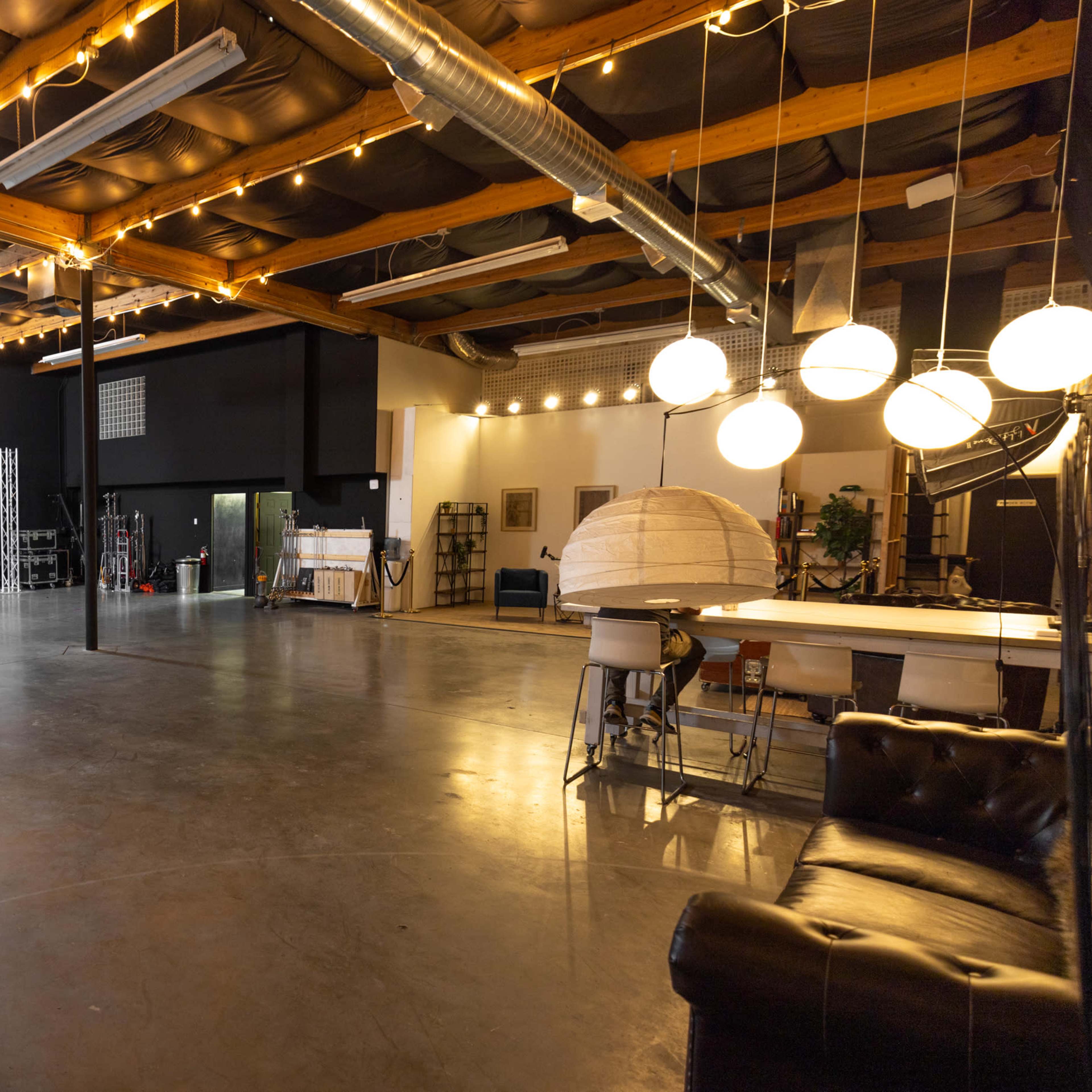 A spacious studio interior with wooden beams, industrial-style lighting, and various set pieces arranged along the walls.
