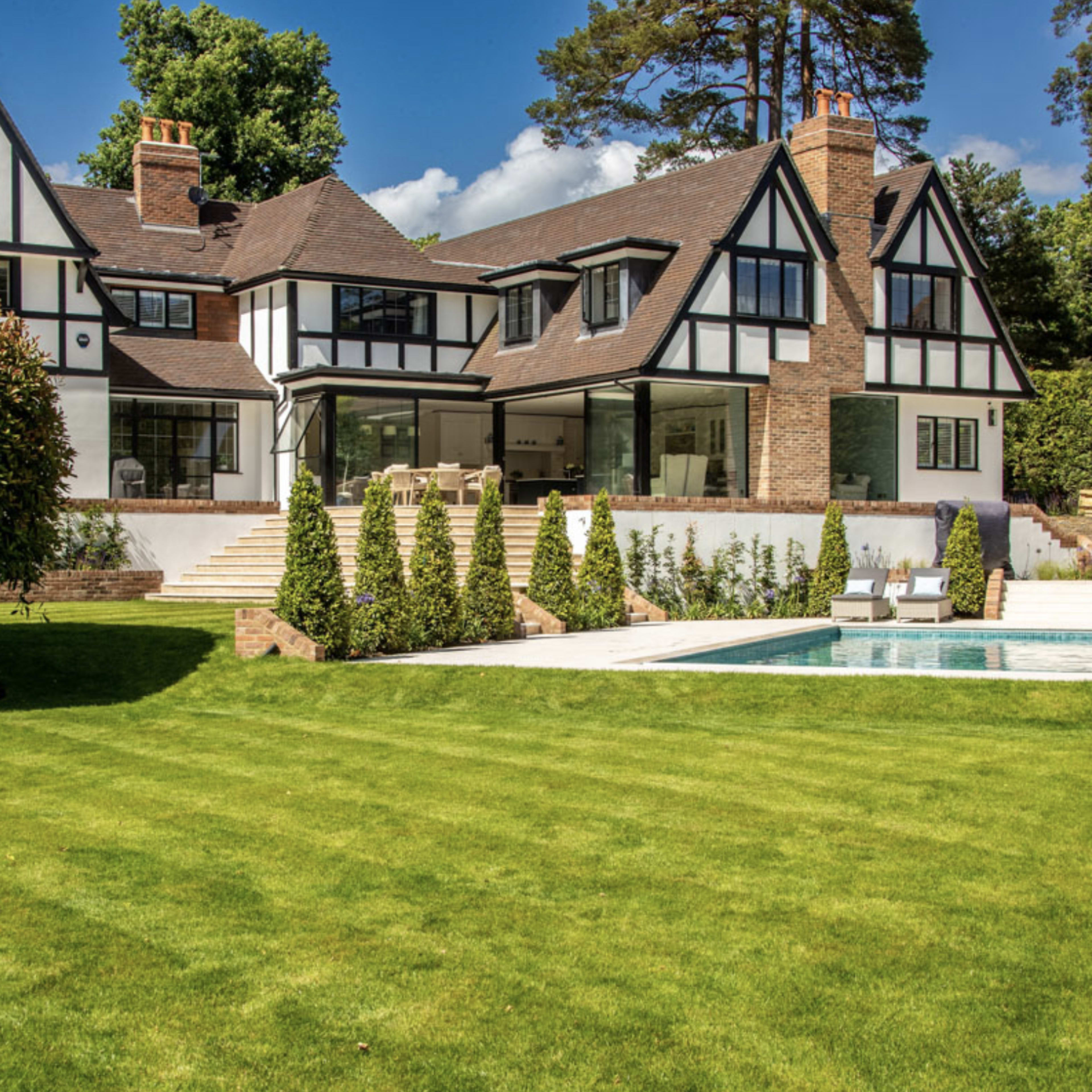 A large, two-story house with a distinct architectural style and a swimming pool surrounded by a well-maintained lawn.
