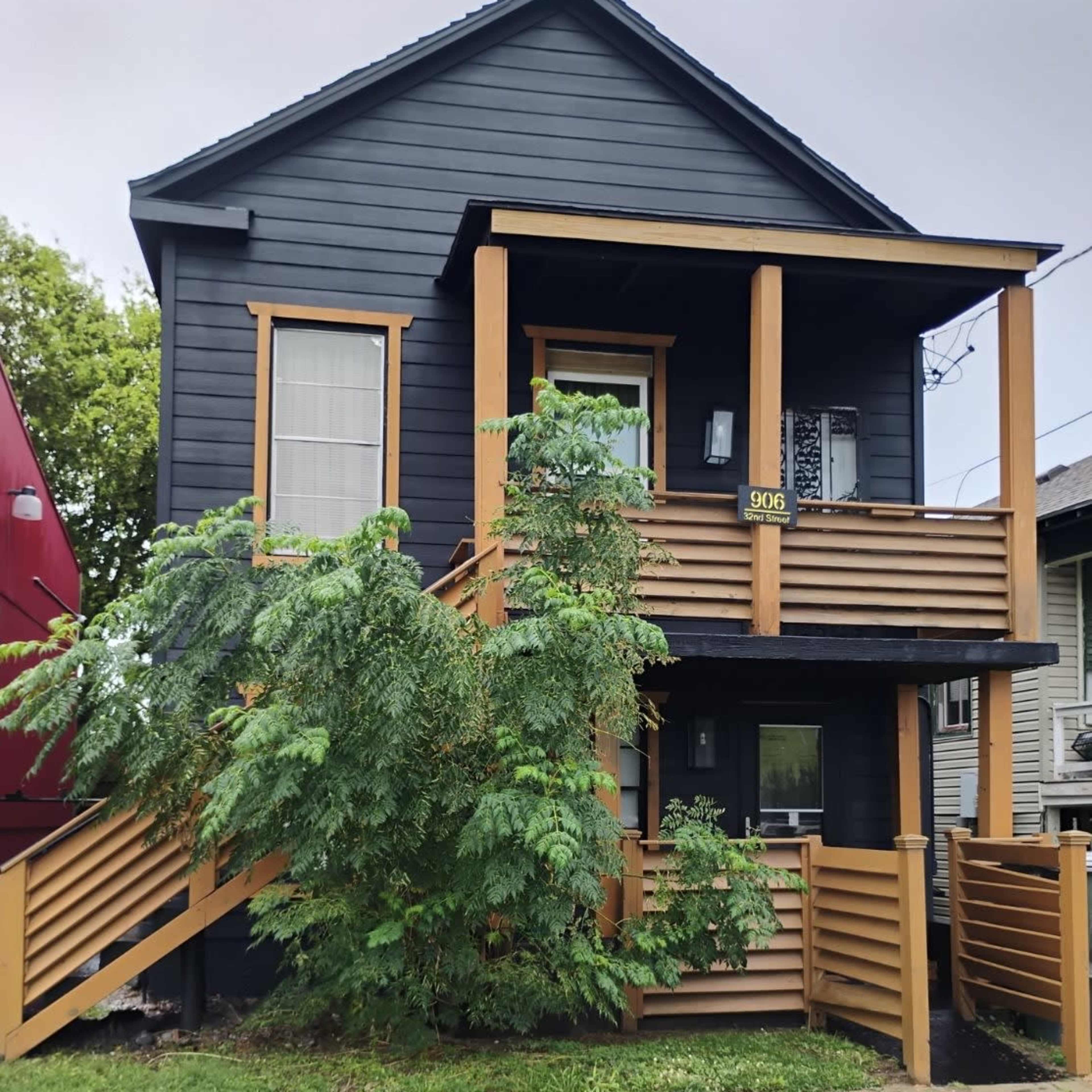 A two-story black house features wooden accents and a front porch with steps leading up to the entrance.