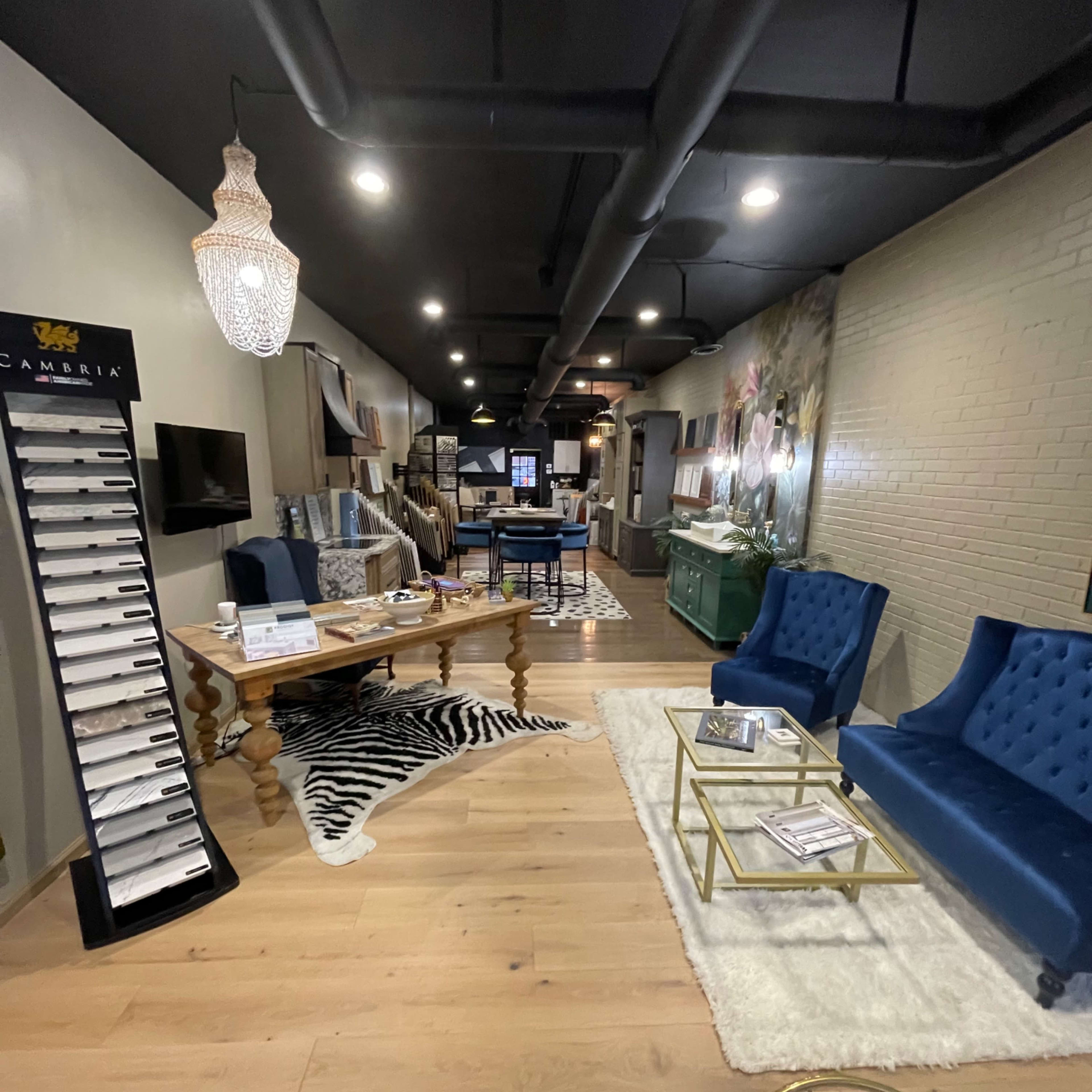 A modern interior space featuring blue upholstered chairs, a wooden table, and a display stand along with decorative elements like rugs and wall art.
