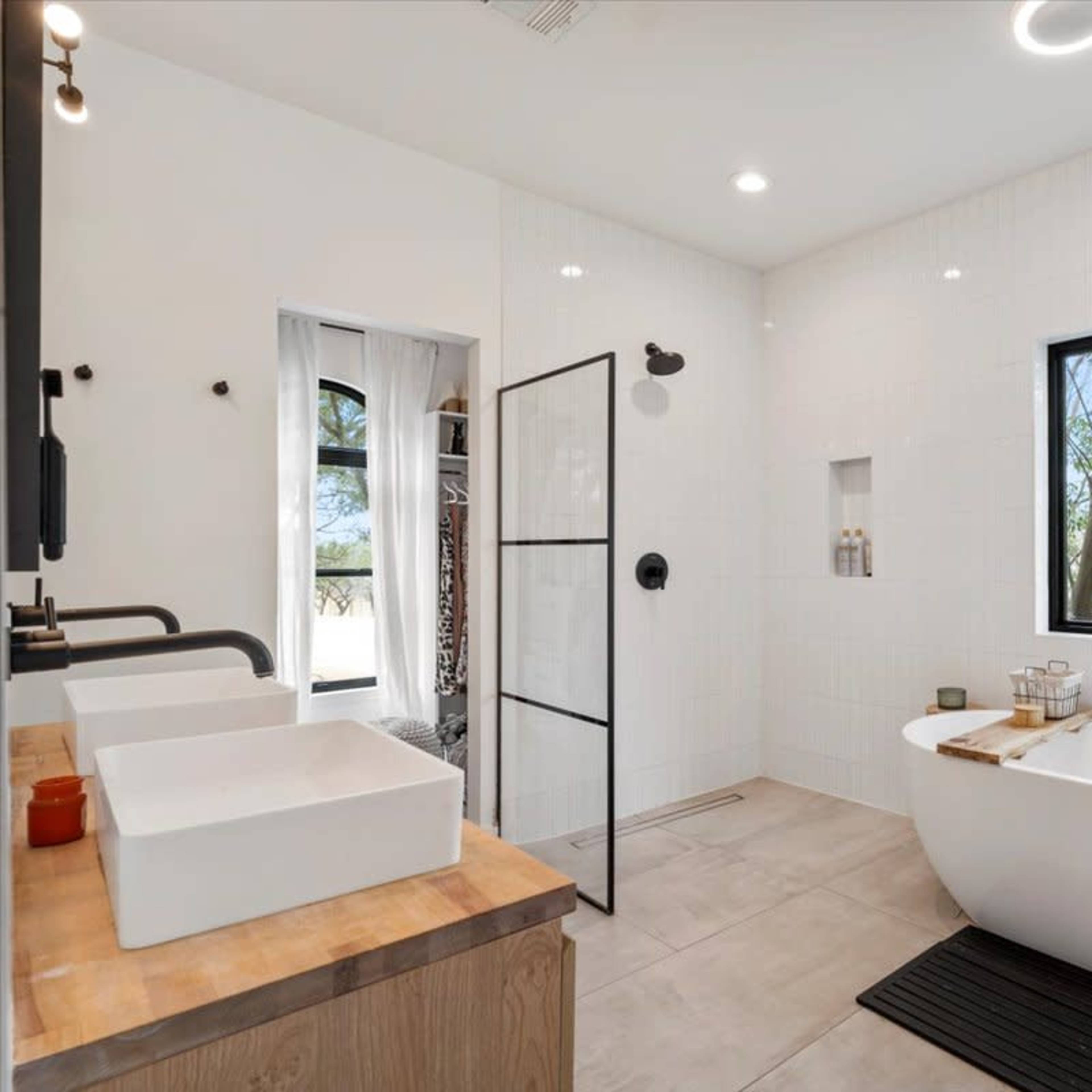A modern bathroom featuring a freestanding bathtub, a double sink with a wooden countertop, and a large window with a view of trees outside.