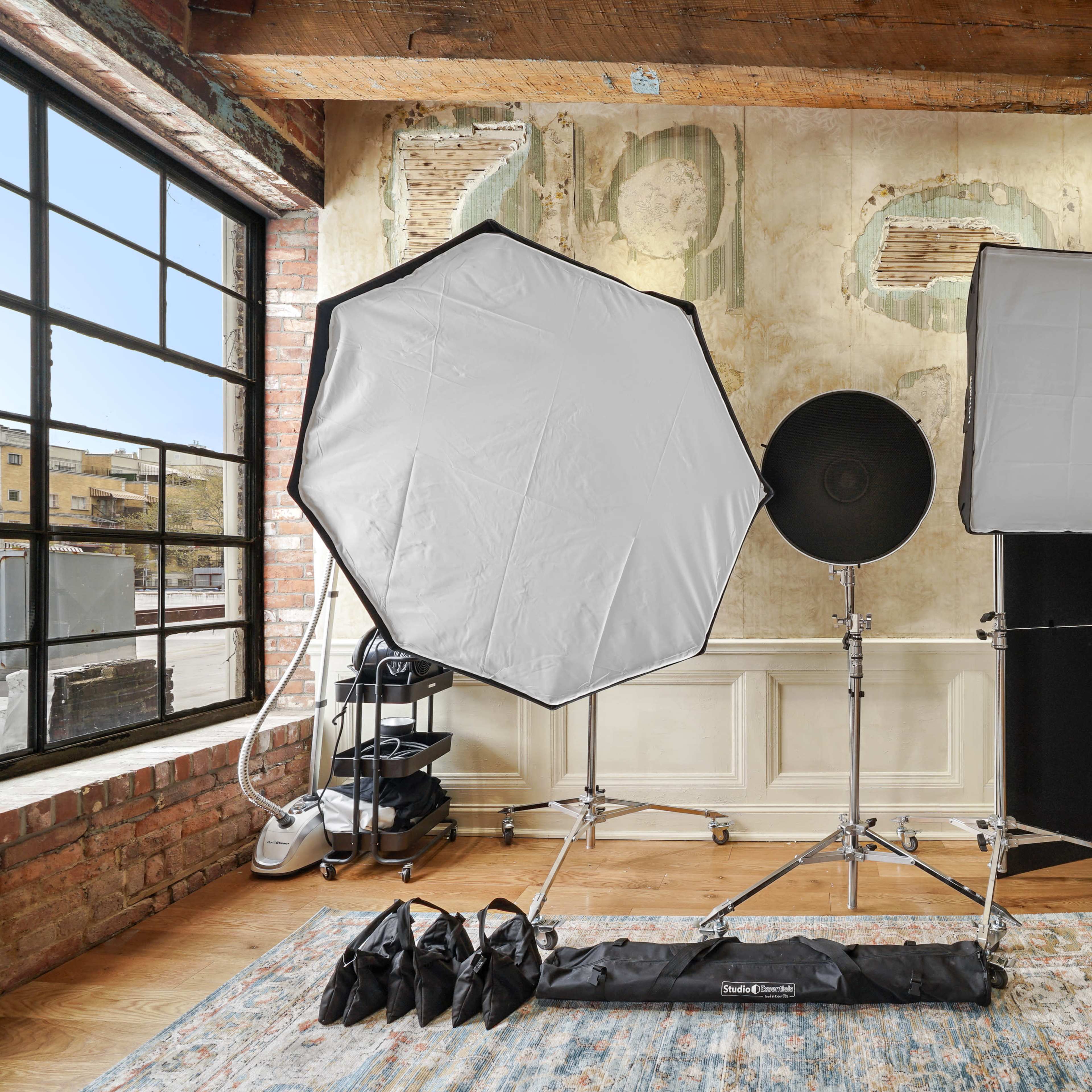 A photography setup featuring softbox lights and a reflector in a room with exposed brick walls and large windows.