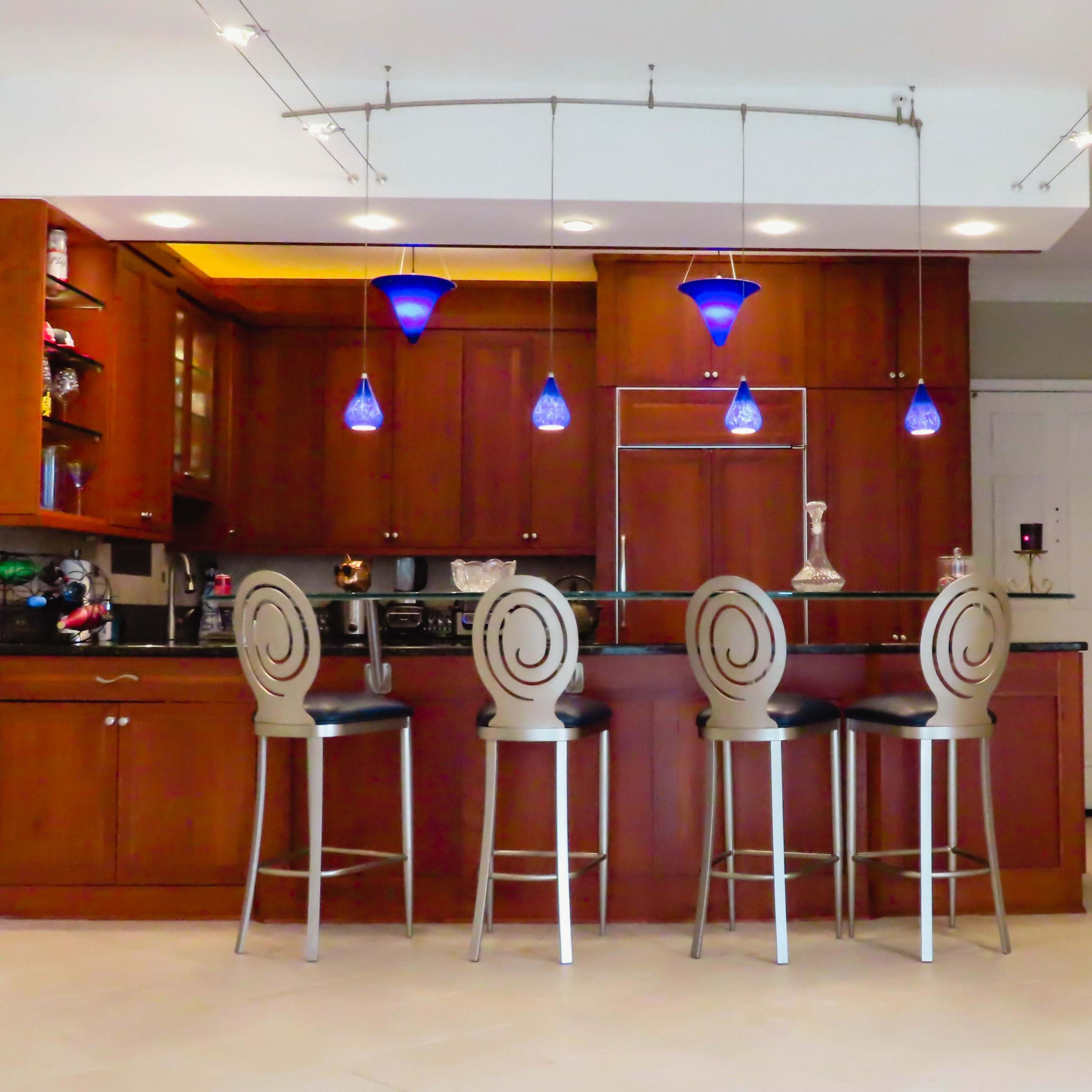 A modern kitchen with wooden cabinetry, a bar counter with four stools, and blue pendant lights above.