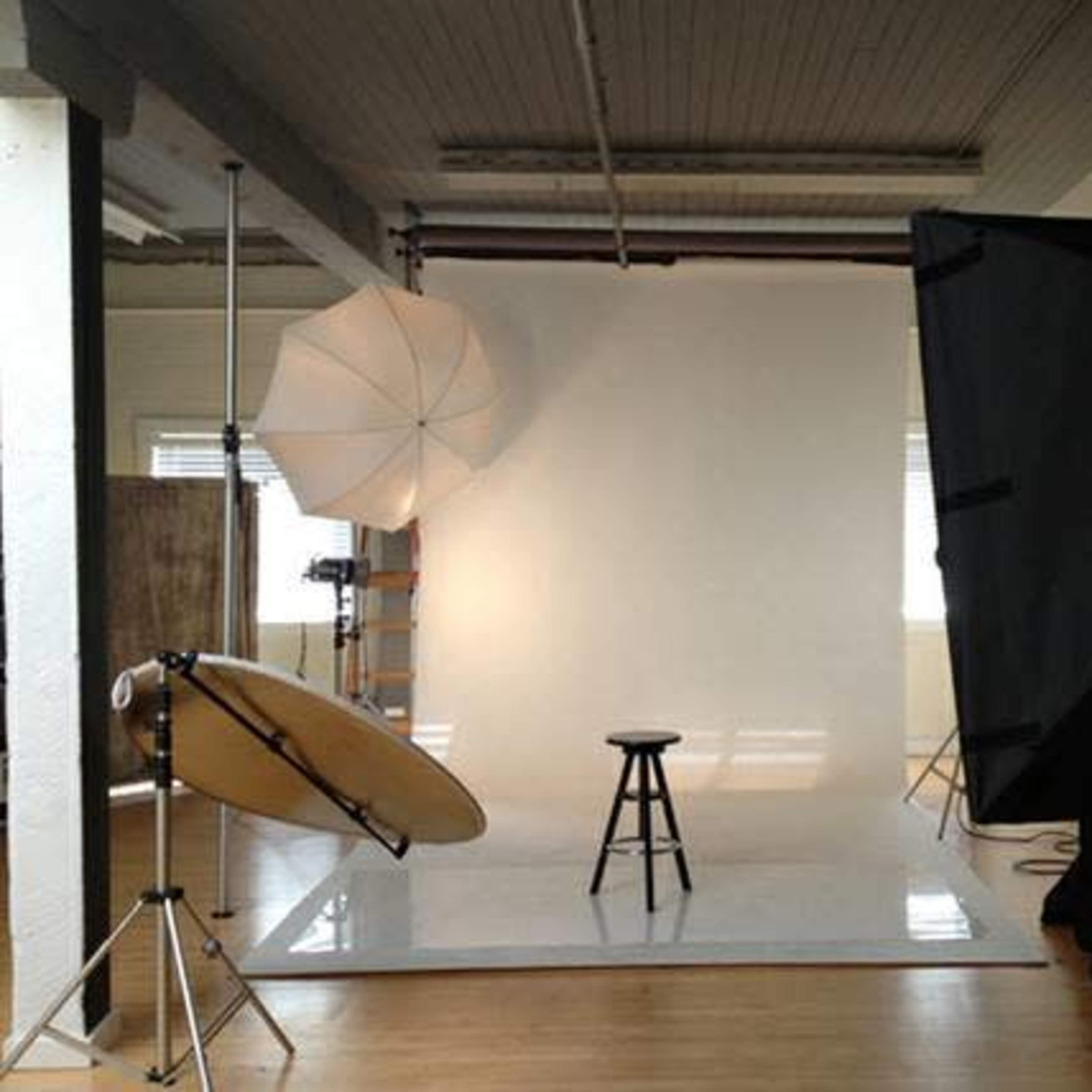 A photography studio with a white backdrop, a stool in the center, and lighting equipment set up on either side.