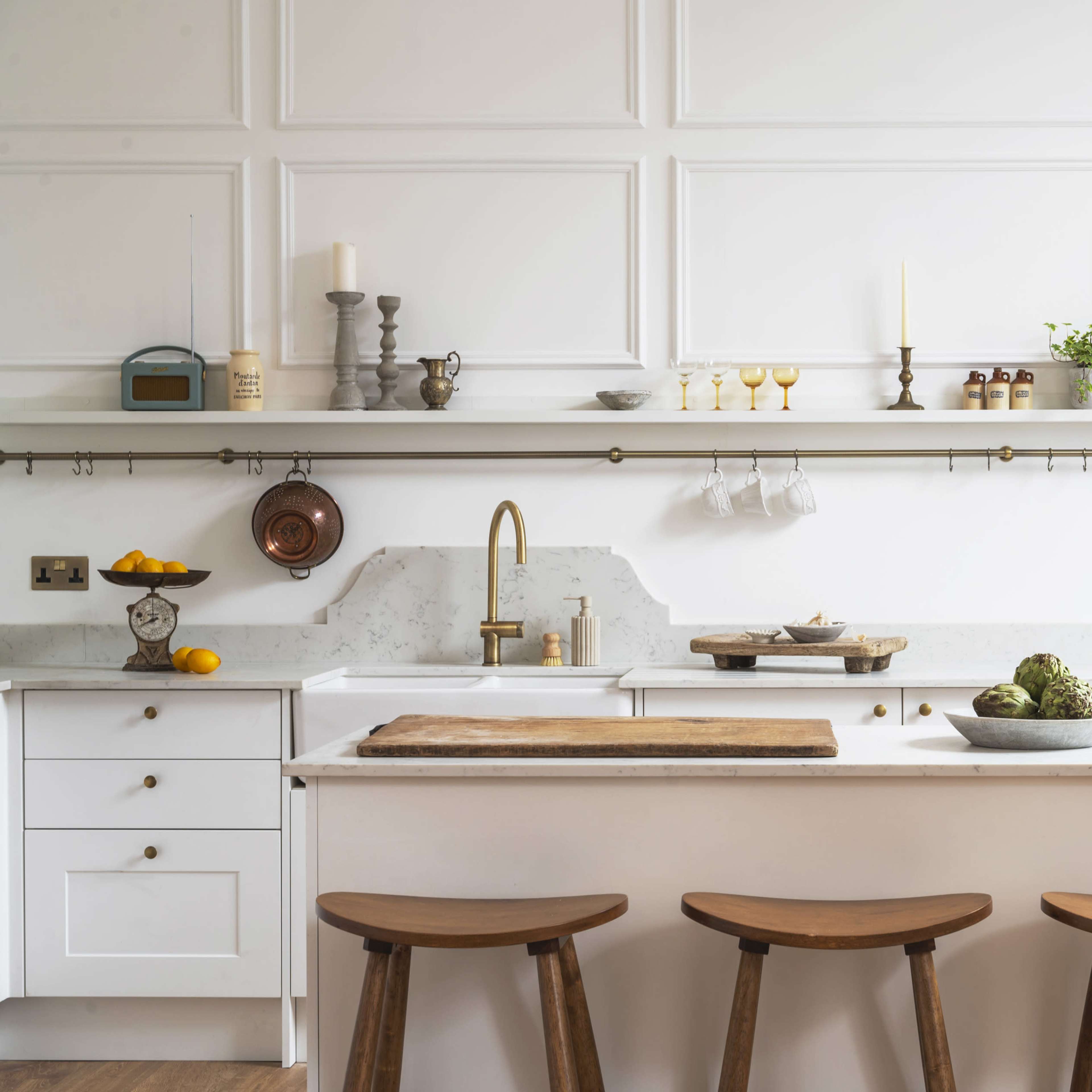 A modern kitchen features white cabinetry, a central island with wooden stools, and a variety of utensils and decorative items neatly arranged on open shelves.