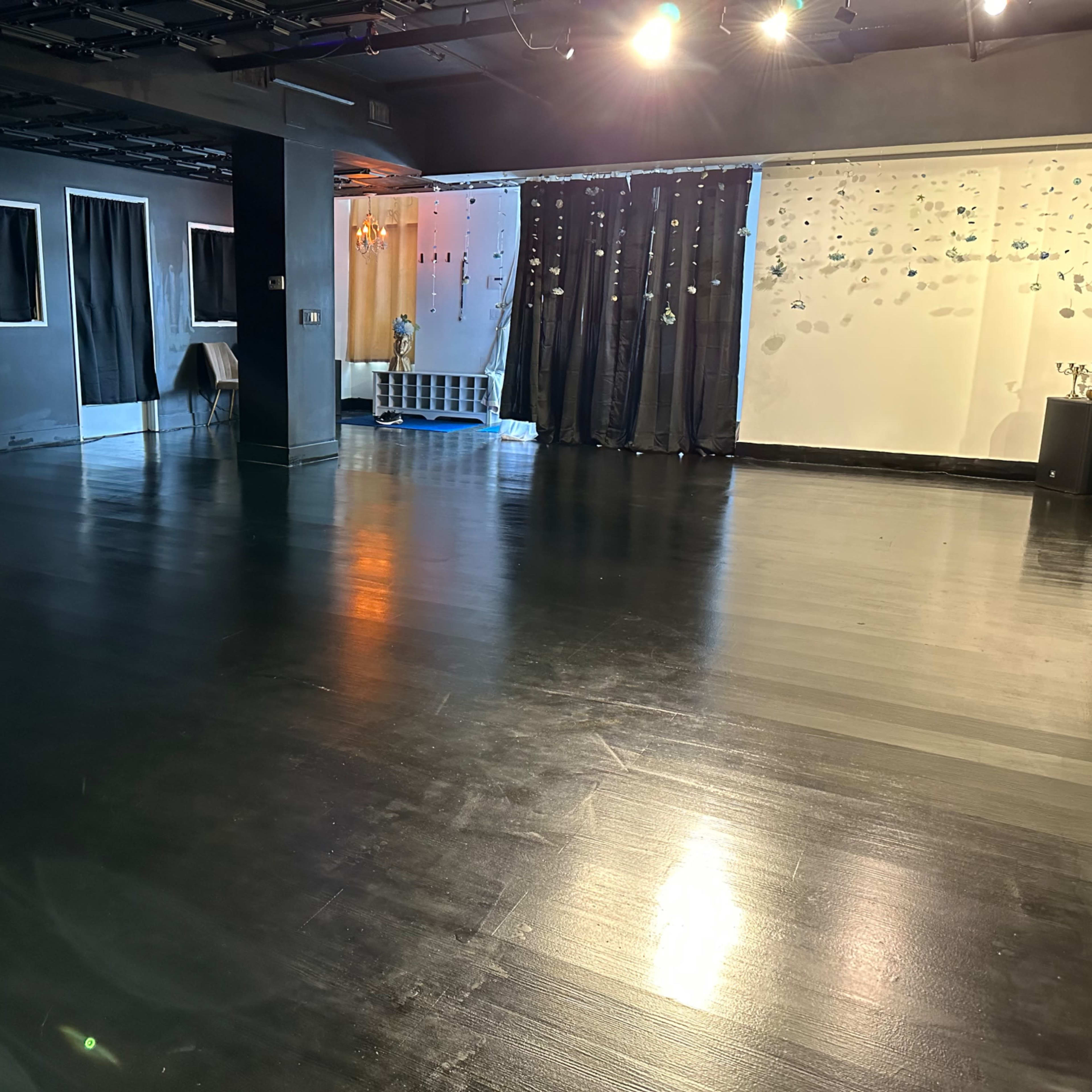 An empty room with a polished black floor, partially covered windows, and a wall decorated with hanging items.