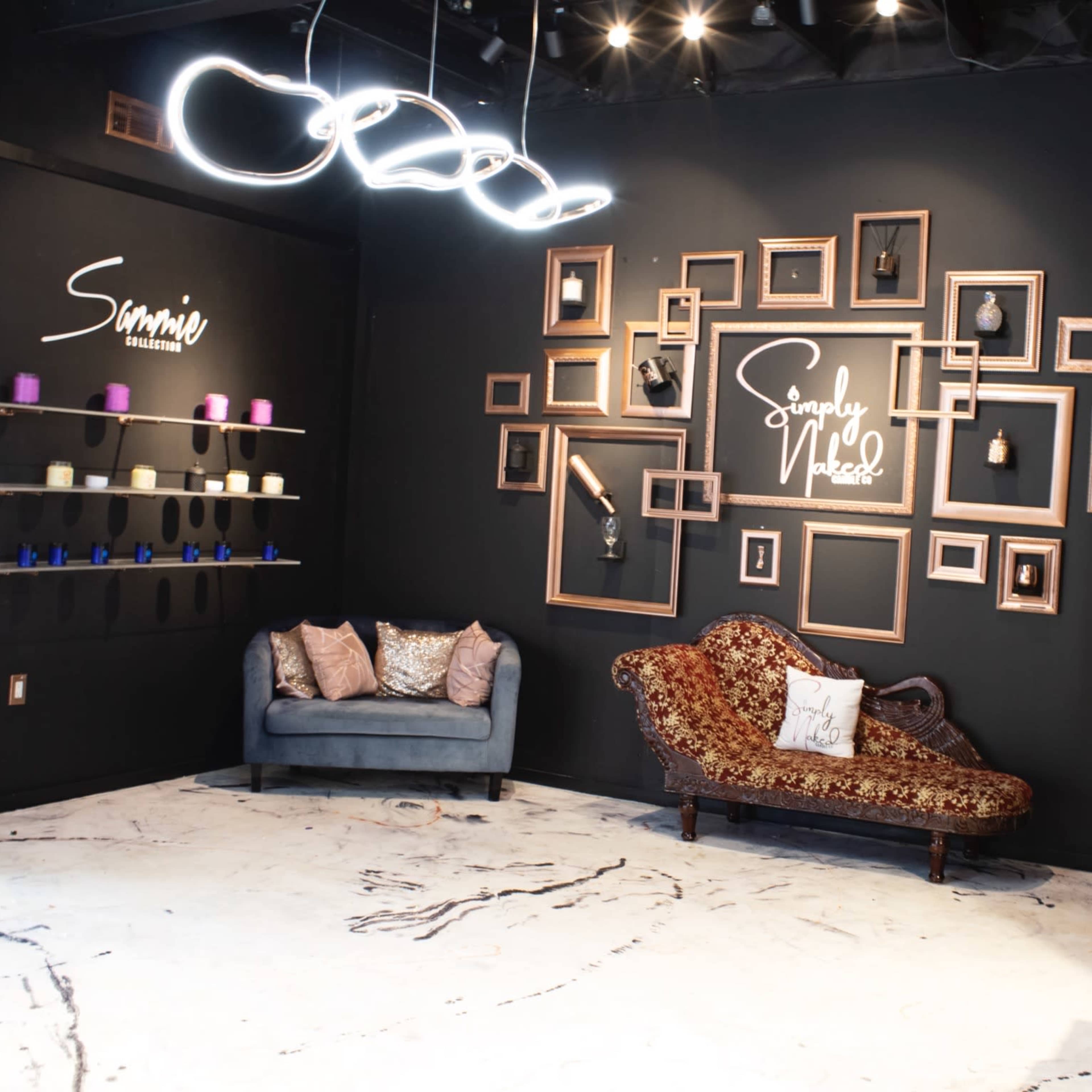 A modern interior space with black walls, featuring a seating area with a couch, a gallery wall of framed pictures, and decorative shelves with candles.