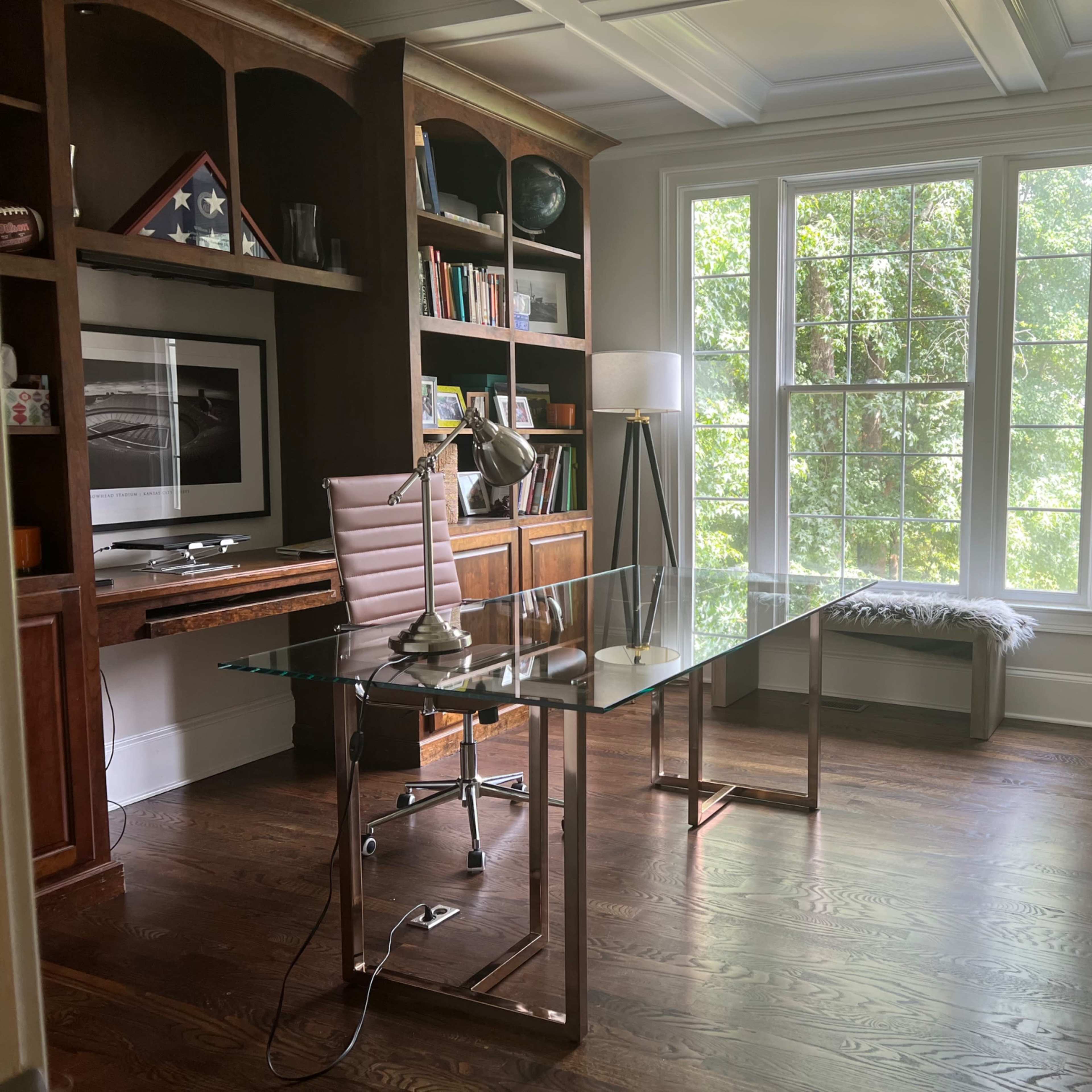 A modern home office with a glass desk, an ergonomic chair, and a large window that allows natural light to illuminate the space.
