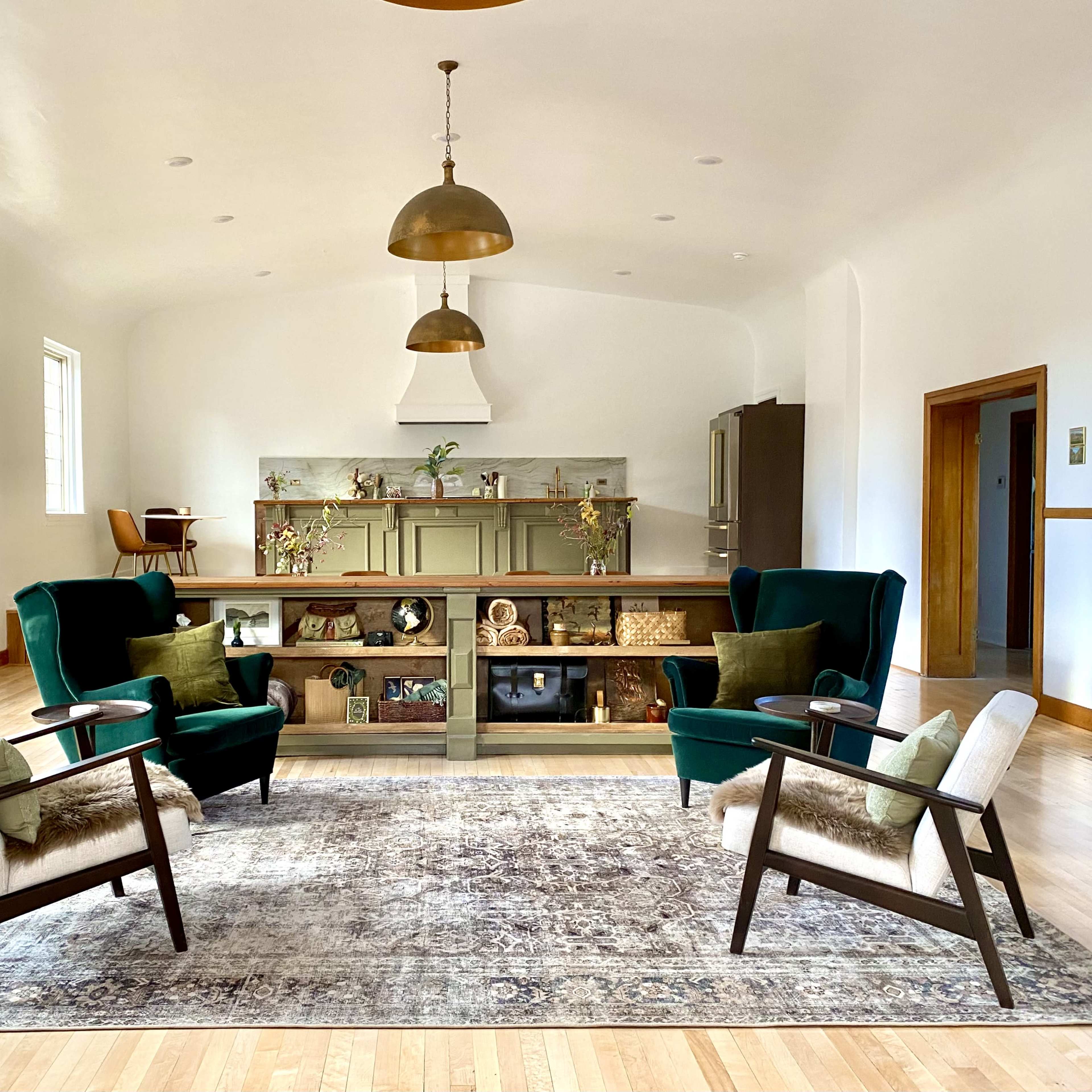 A spacious living room with two green armchairs and a light rug, centered around a wooden display unit against a white wall.