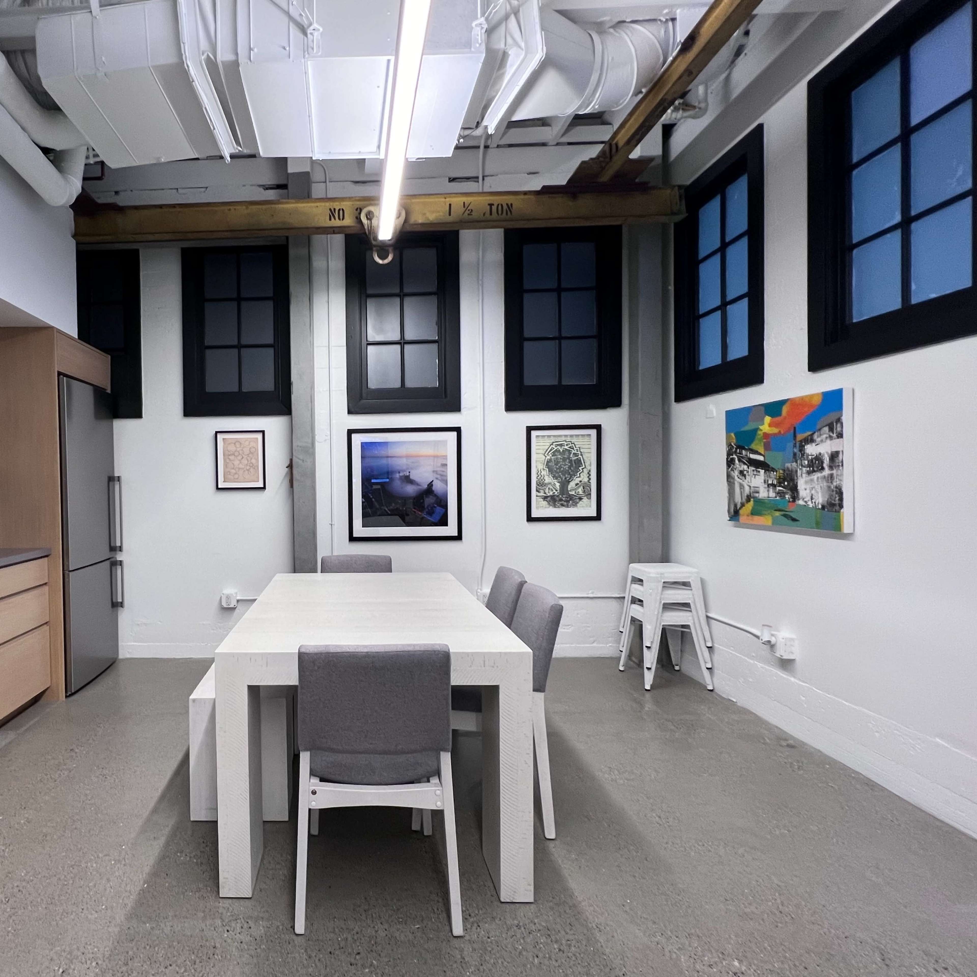 A modern kitchen with a large white table surrounded by gray chairs, cabinets with plates, and artwork on the walls.