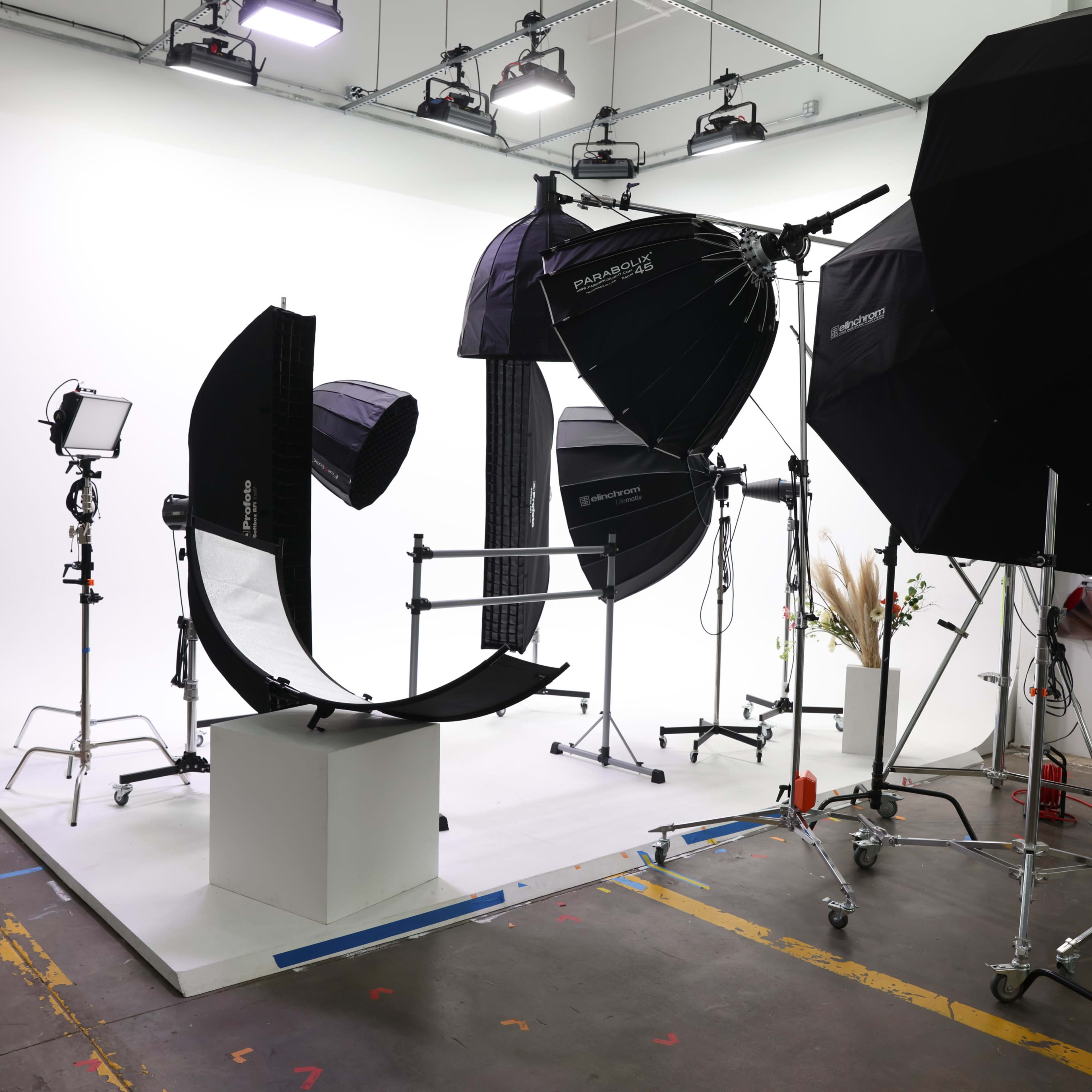 A photography studio setup with multiple light stands, softboxes, and a central display platform against a white backdrop.