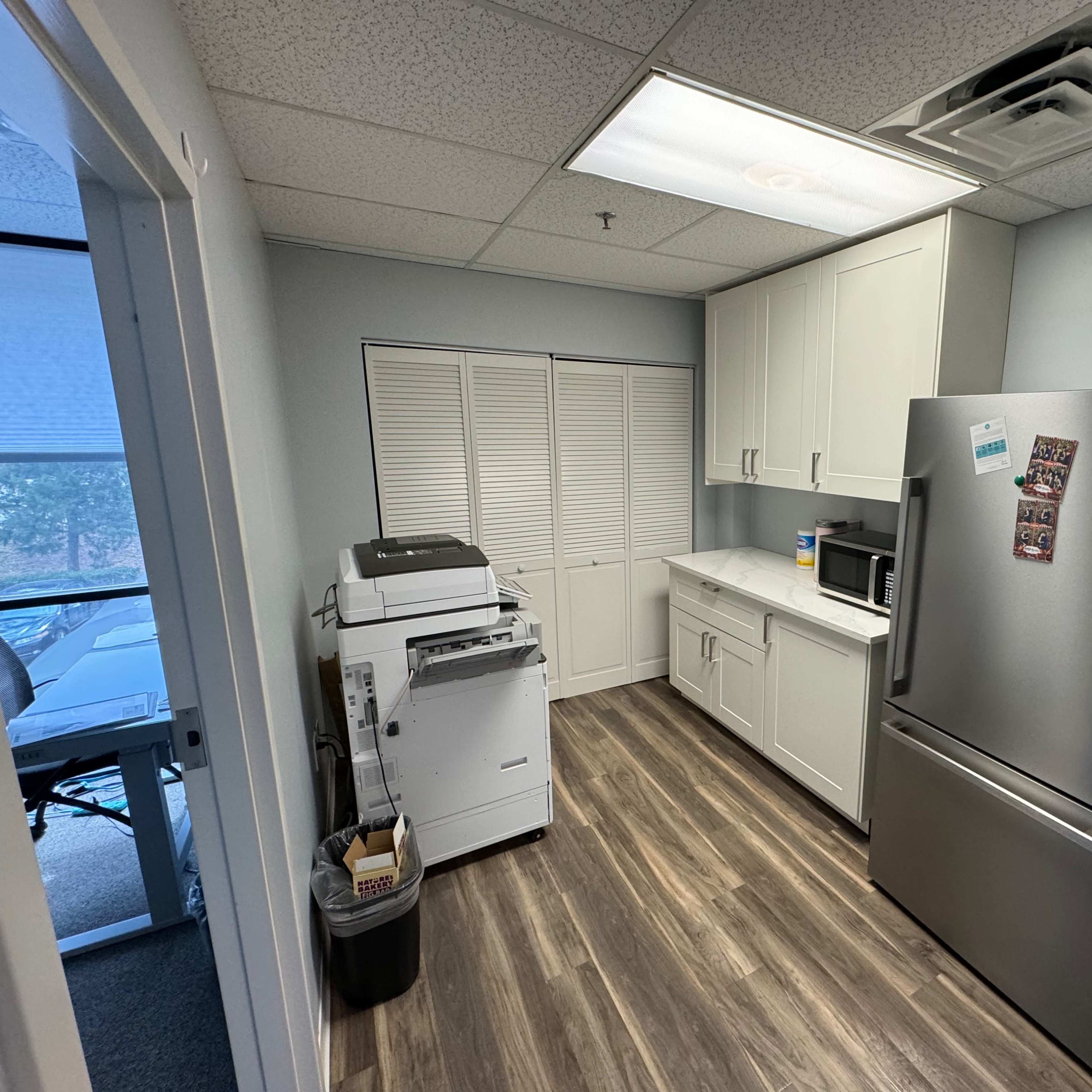 A compact kitchen area featuring a refrigerator, microwave, and a printer next to a white cabinetry setup.