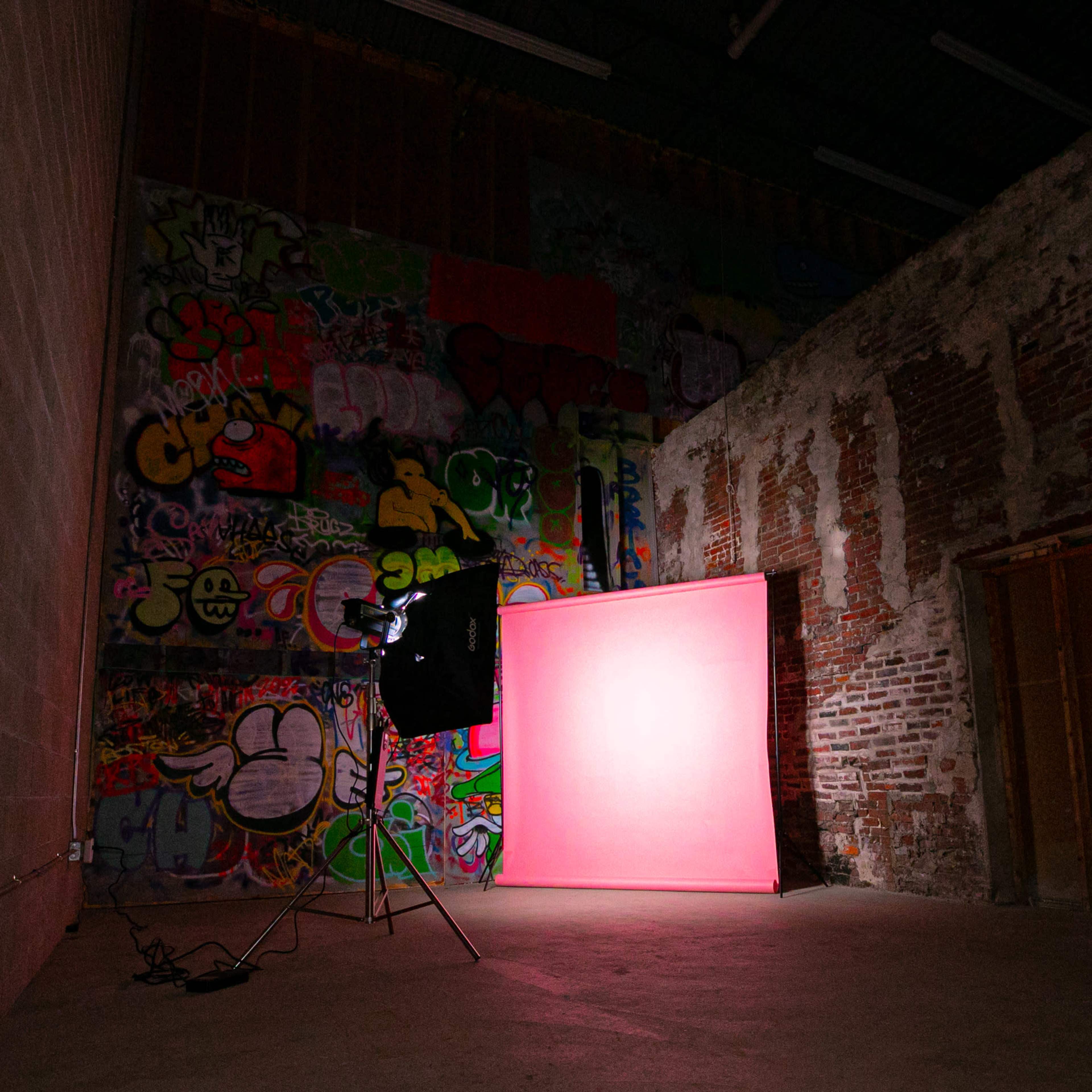 An empty industrial space with a pink backdrop and a light setup against a wall covered in colorful graffiti.