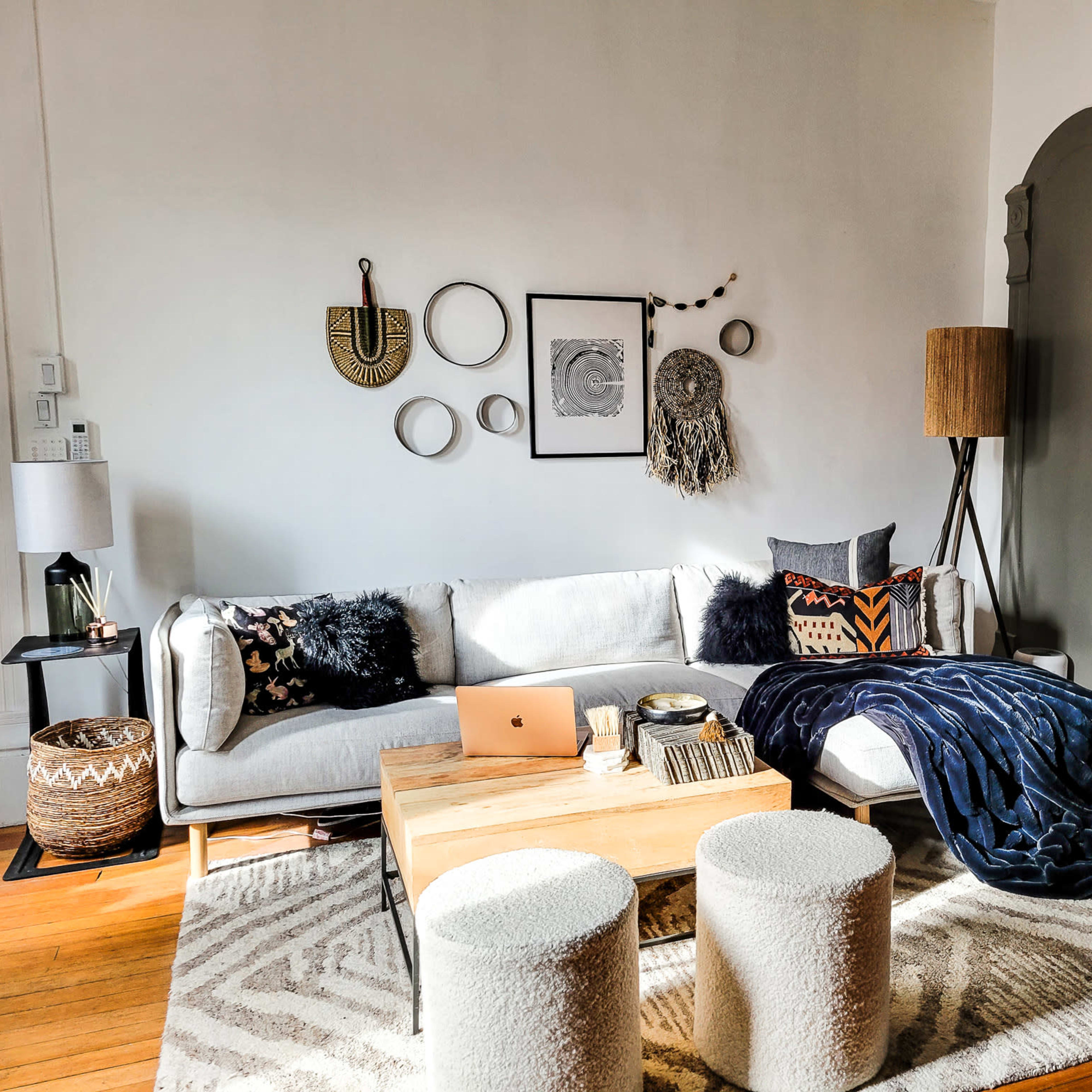 The scene features a modern living room with a gray sofa, a wooden coffee table, two round stools, and various decorative items on the walls.
