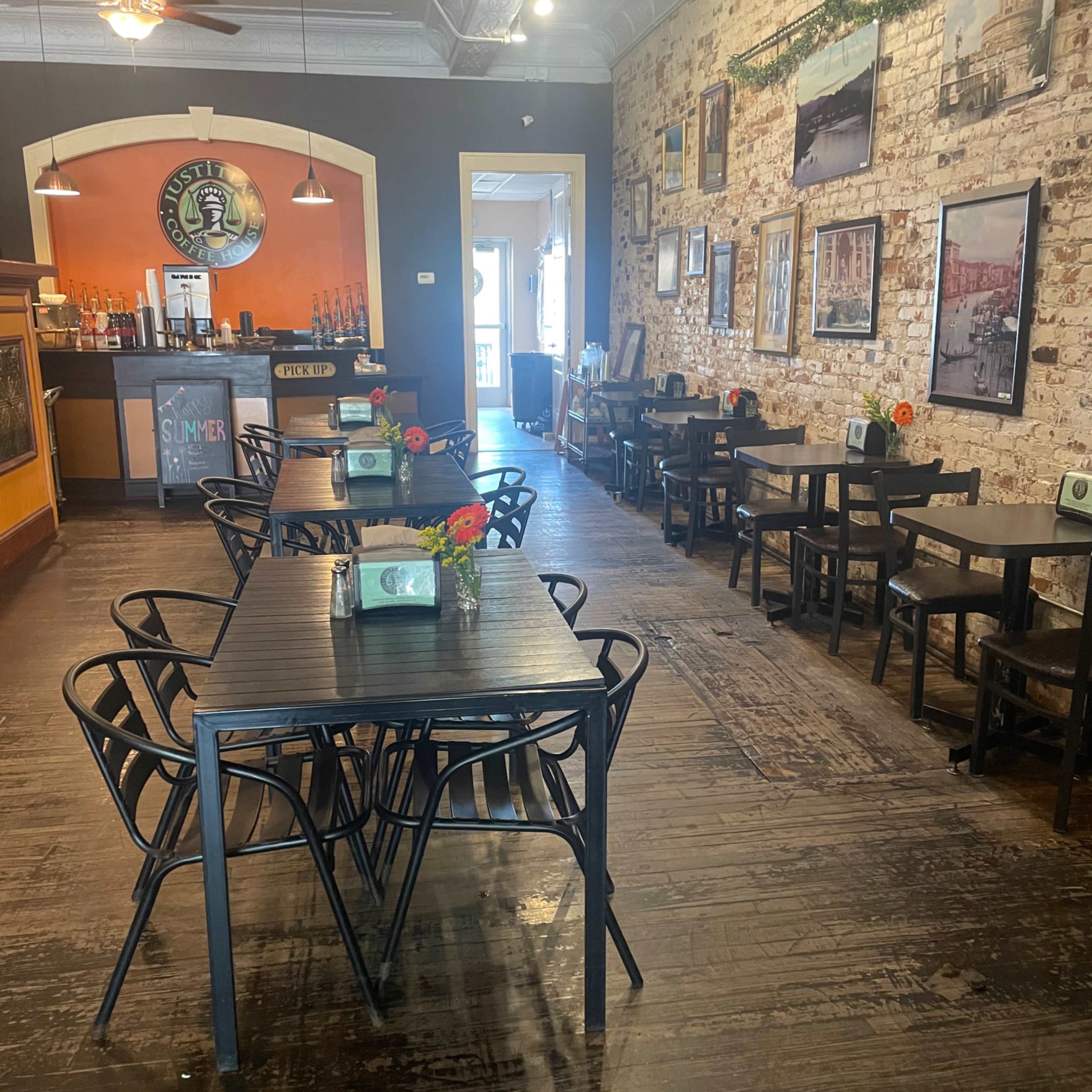 A spacious restaurant features black metal tables and chairs arranged neatly, with a bar in the background and photographs hanging on the walls.