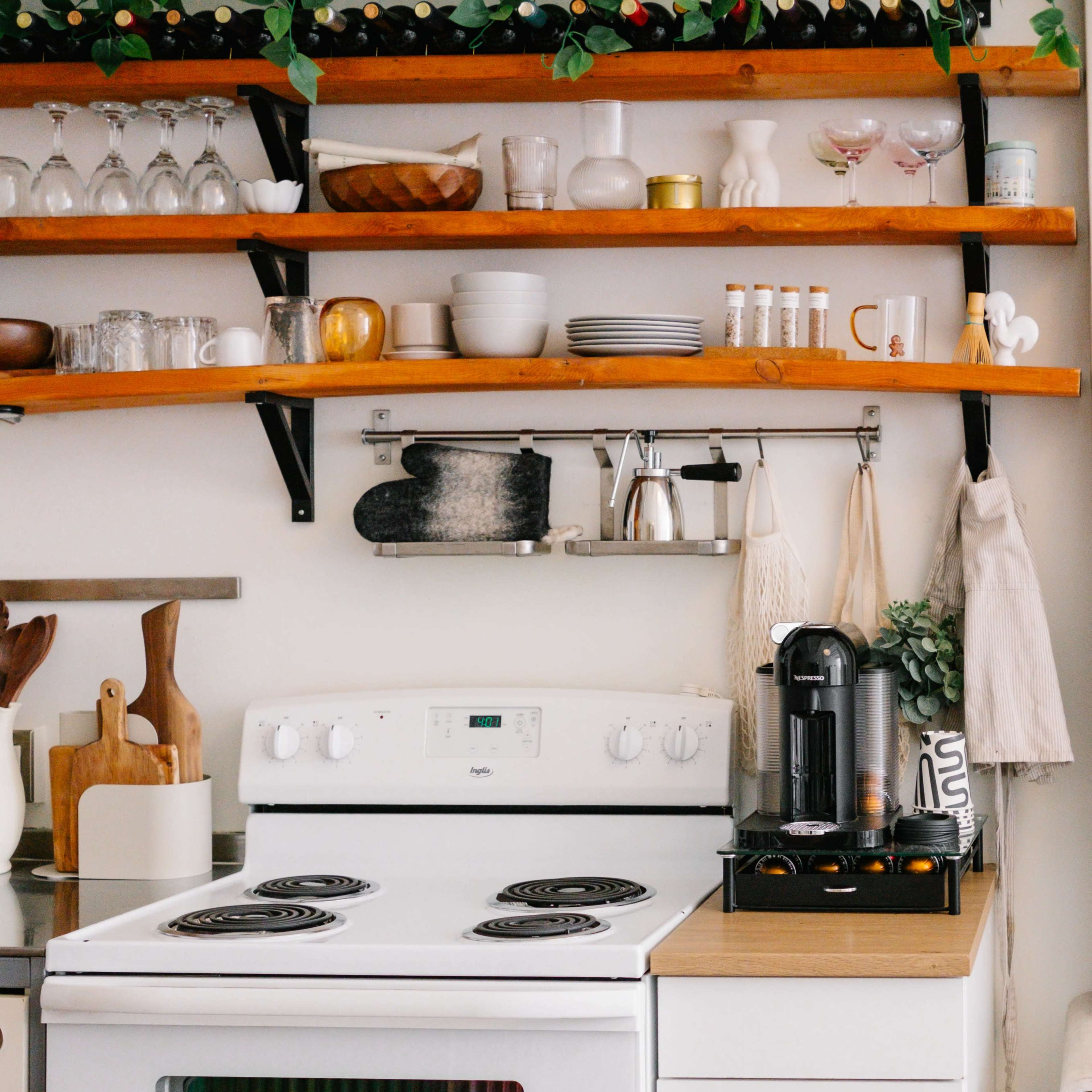 A tidy kitchen with an electric stove, a countertop coffee maker, and open shelves displaying various kitchenware and utensils.