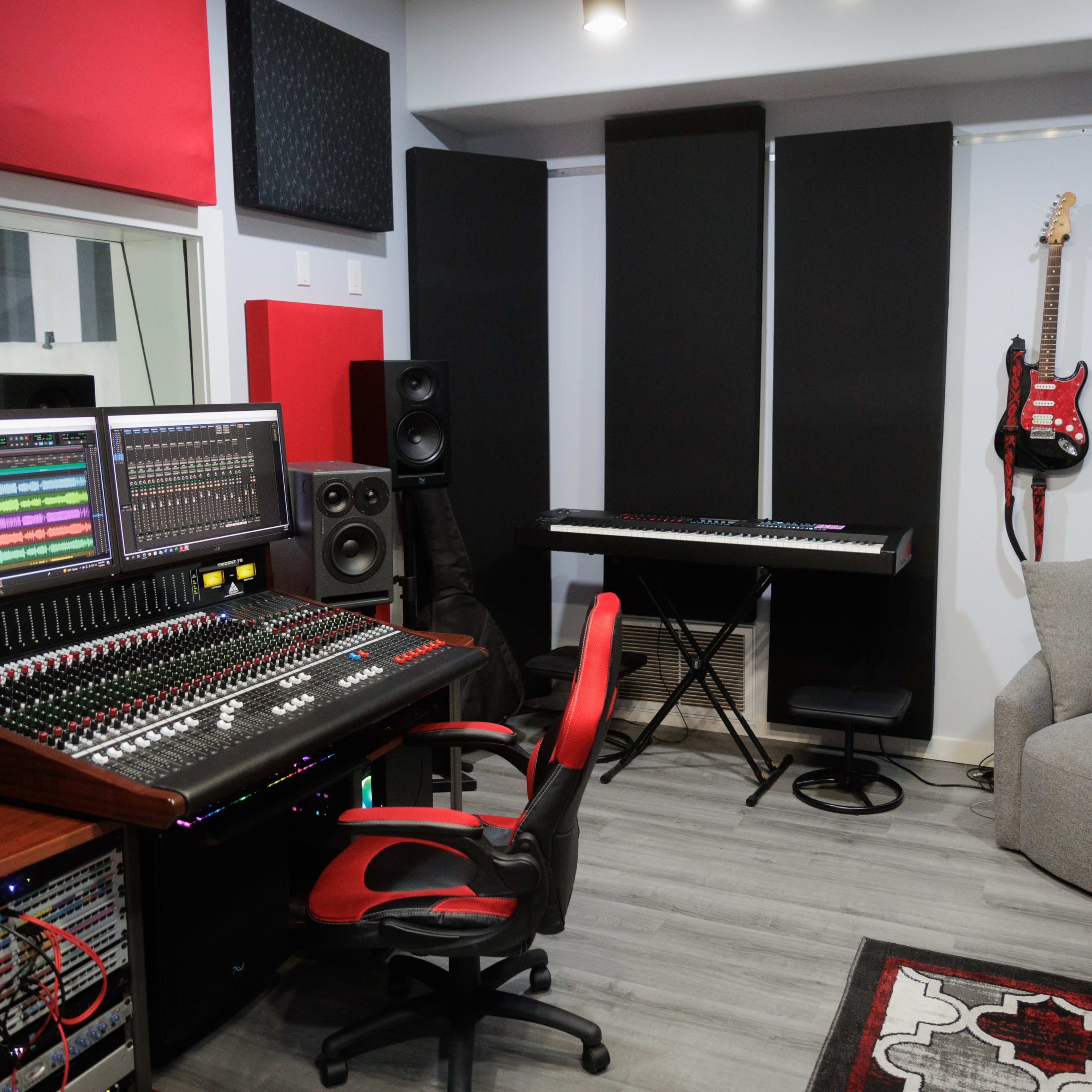 A modern music studio featuring a mixing console, computer screens, a keyboard, and a cozy seating area.