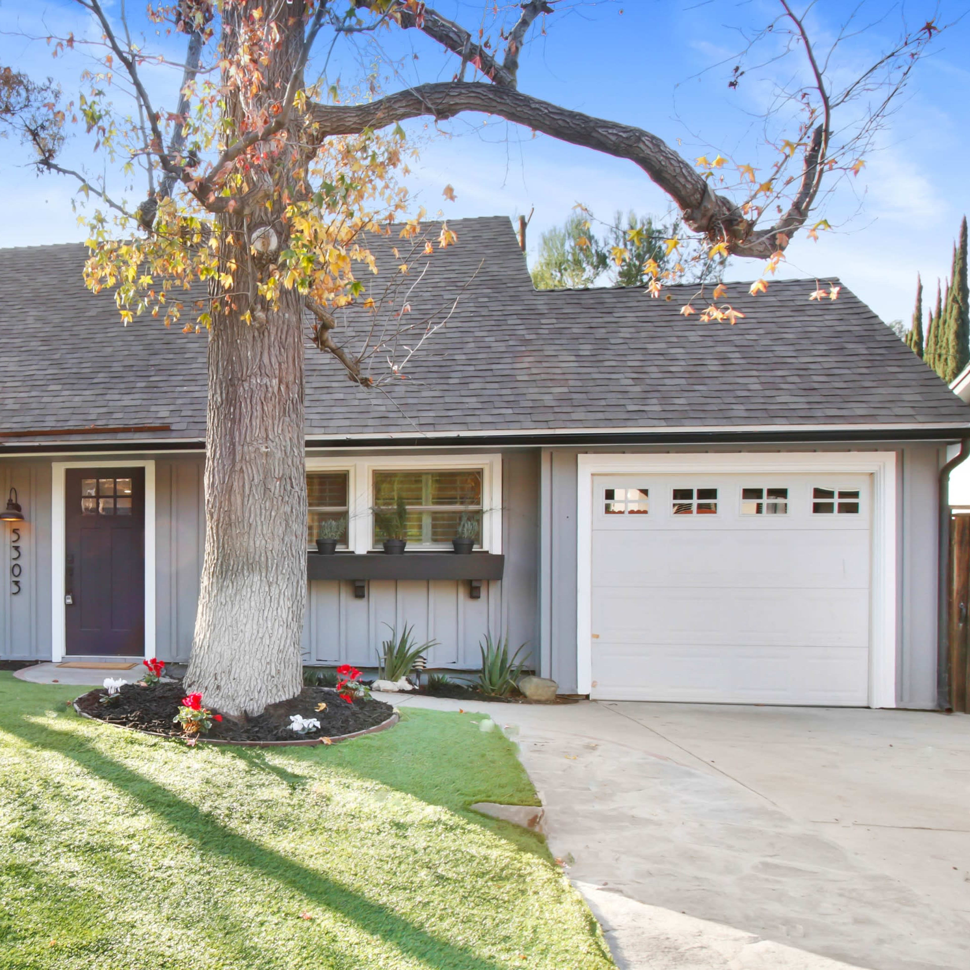 A single-story house with a pitched roof, a front yard featuring grass and flower beds, and a garage on the right.