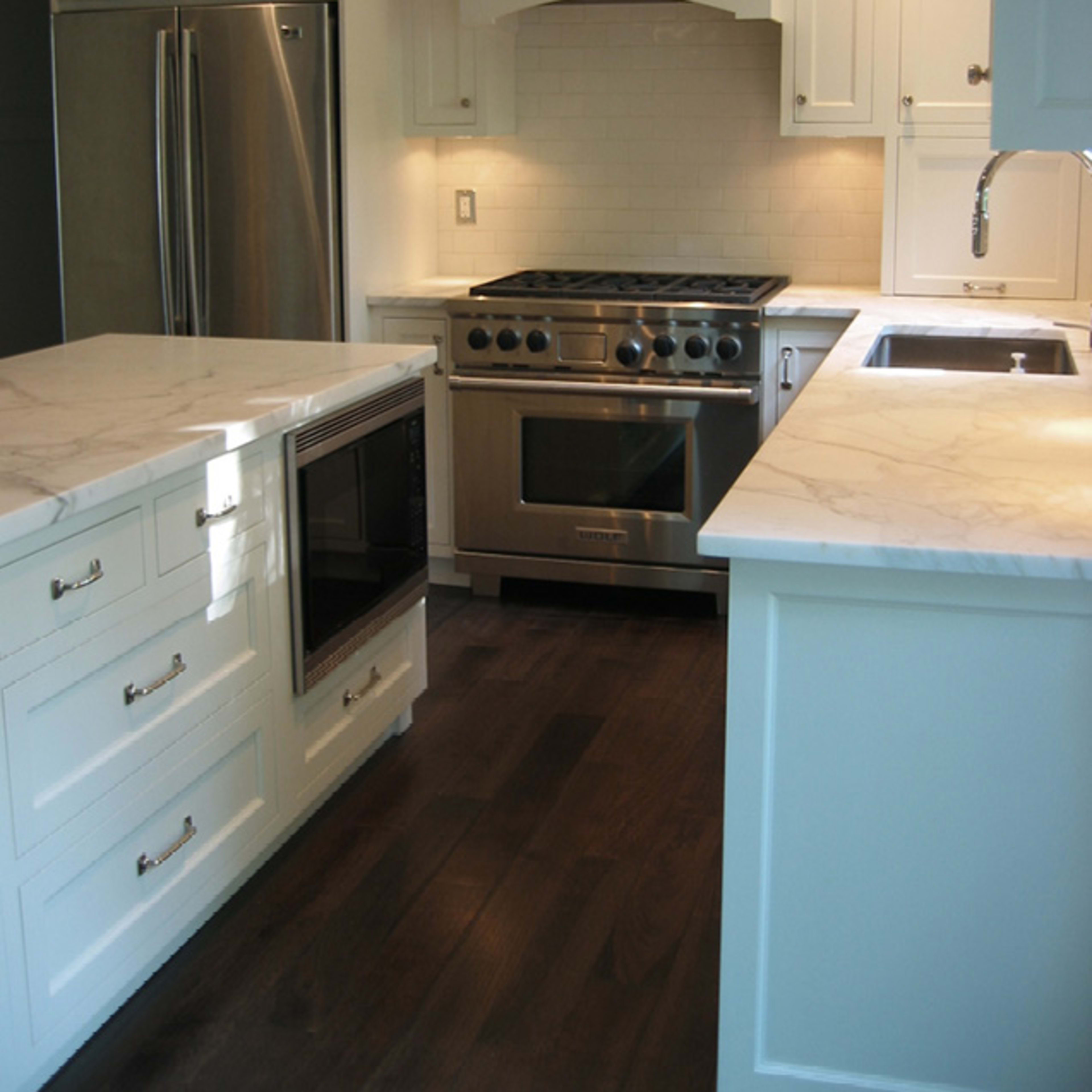 A modern kitchen featuring white cabinetry, marble countertops, and stainless steel appliances.