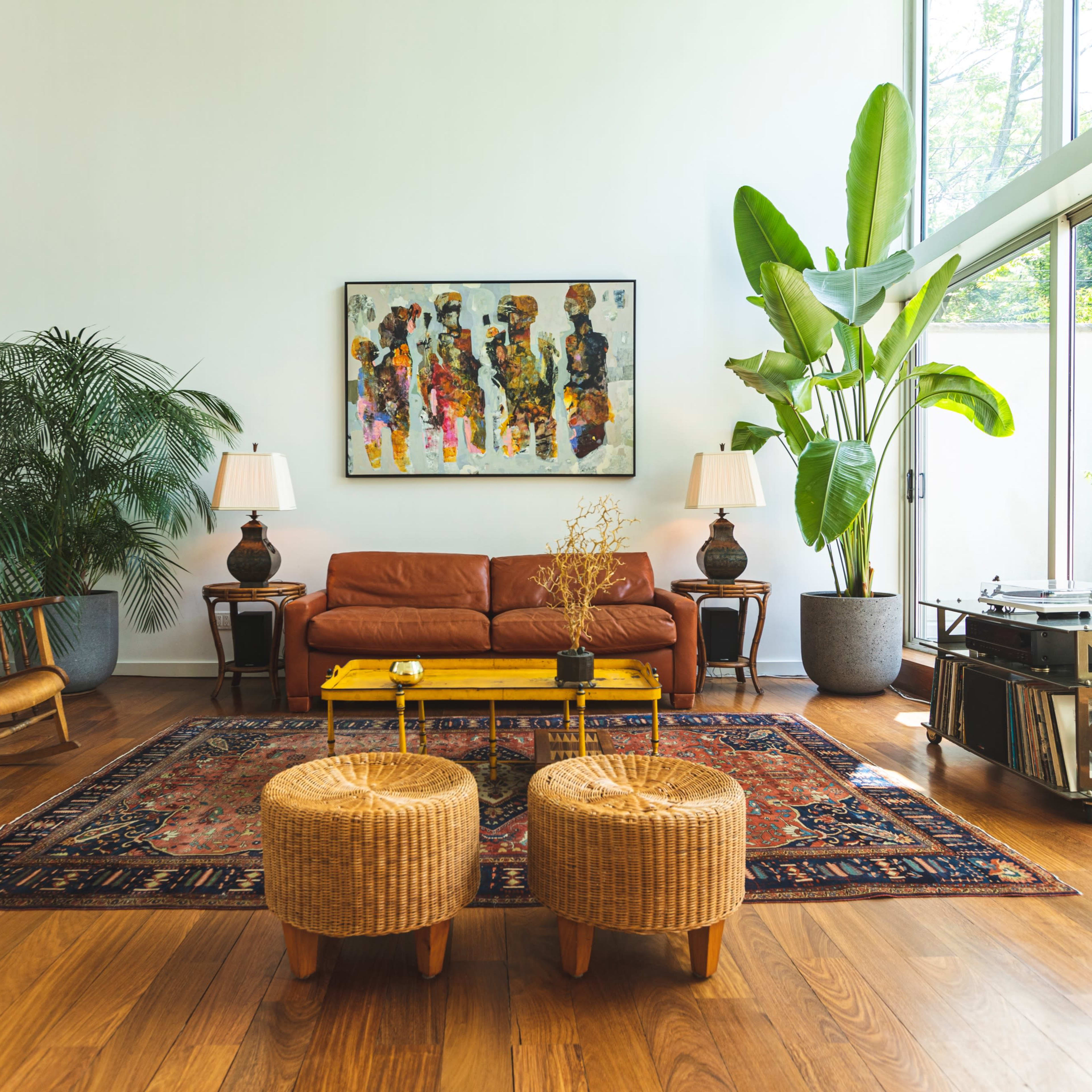 The living room features a modern design with a leather sofa, two wicker stools, and large windows allowing natural light to illuminate the space.