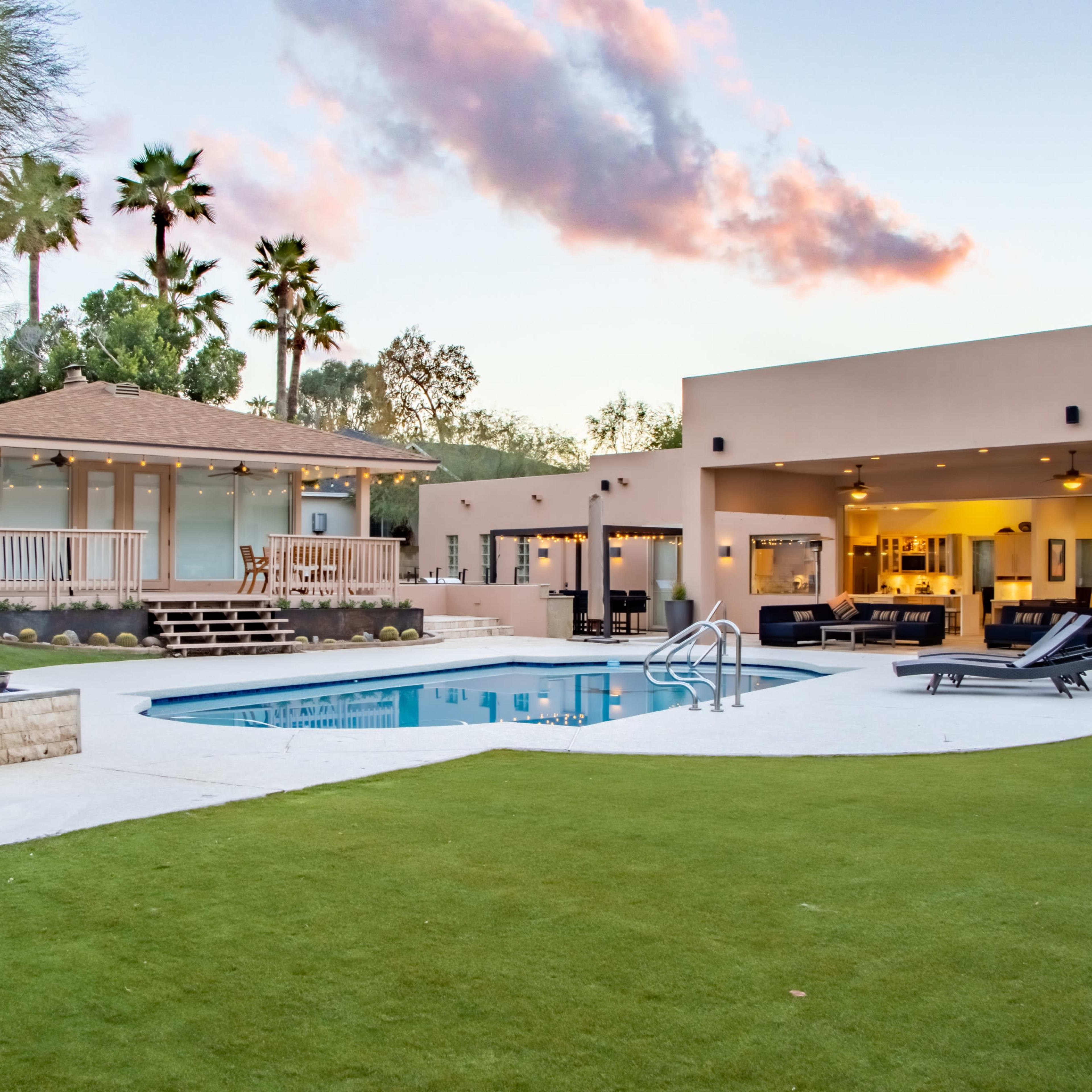 A modern house with a pool, surrounded by well-maintained grass and palm trees, featuring an outdoor terrace and lounge area.