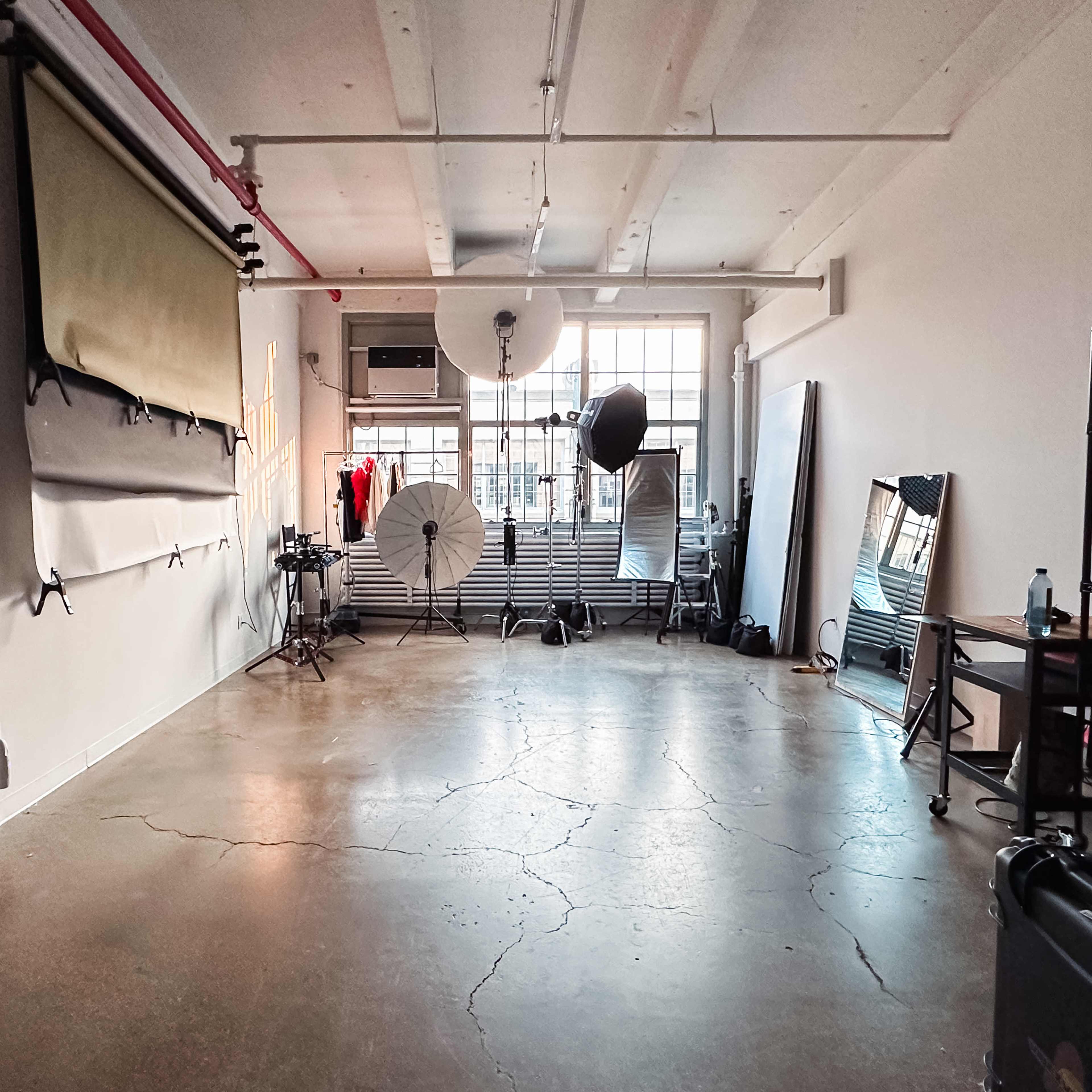 A photography studio with various backdrops, lighting equipment, and a large window allowing natural light.