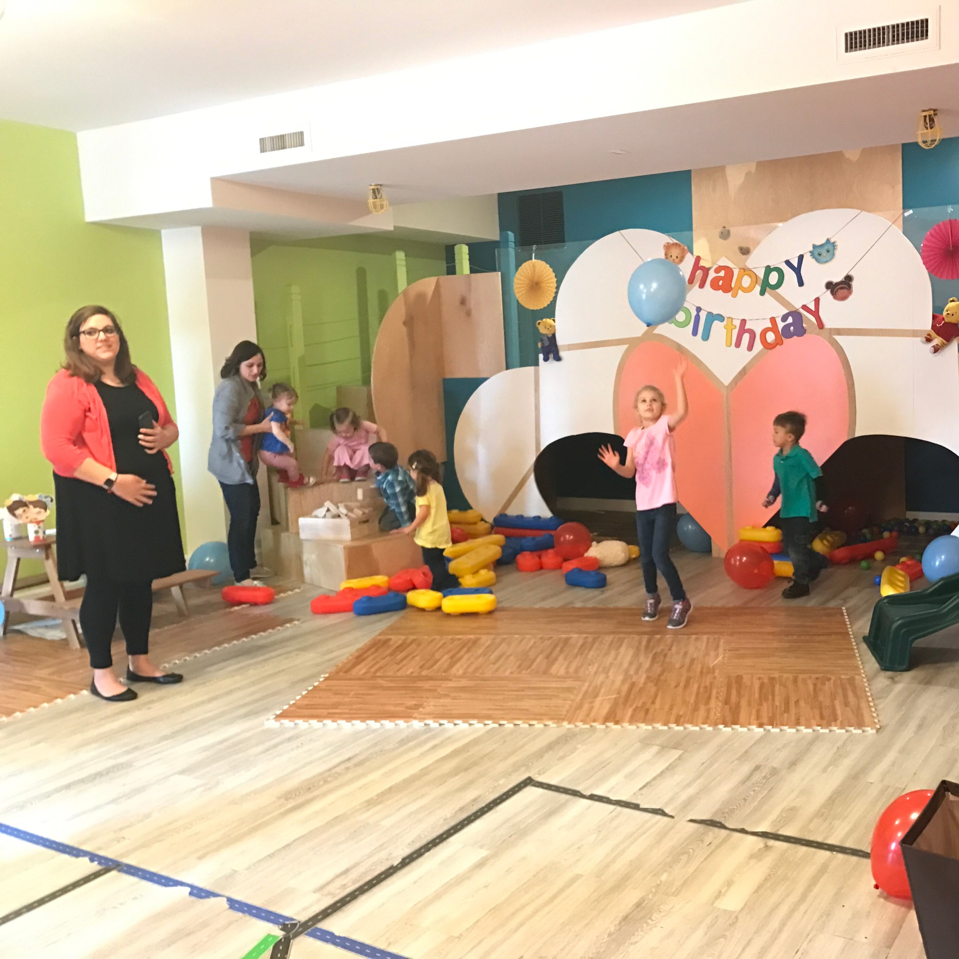 A colorful birthday party scene features children playing with balloons and toys, while adults supervise in a decorated indoor space.