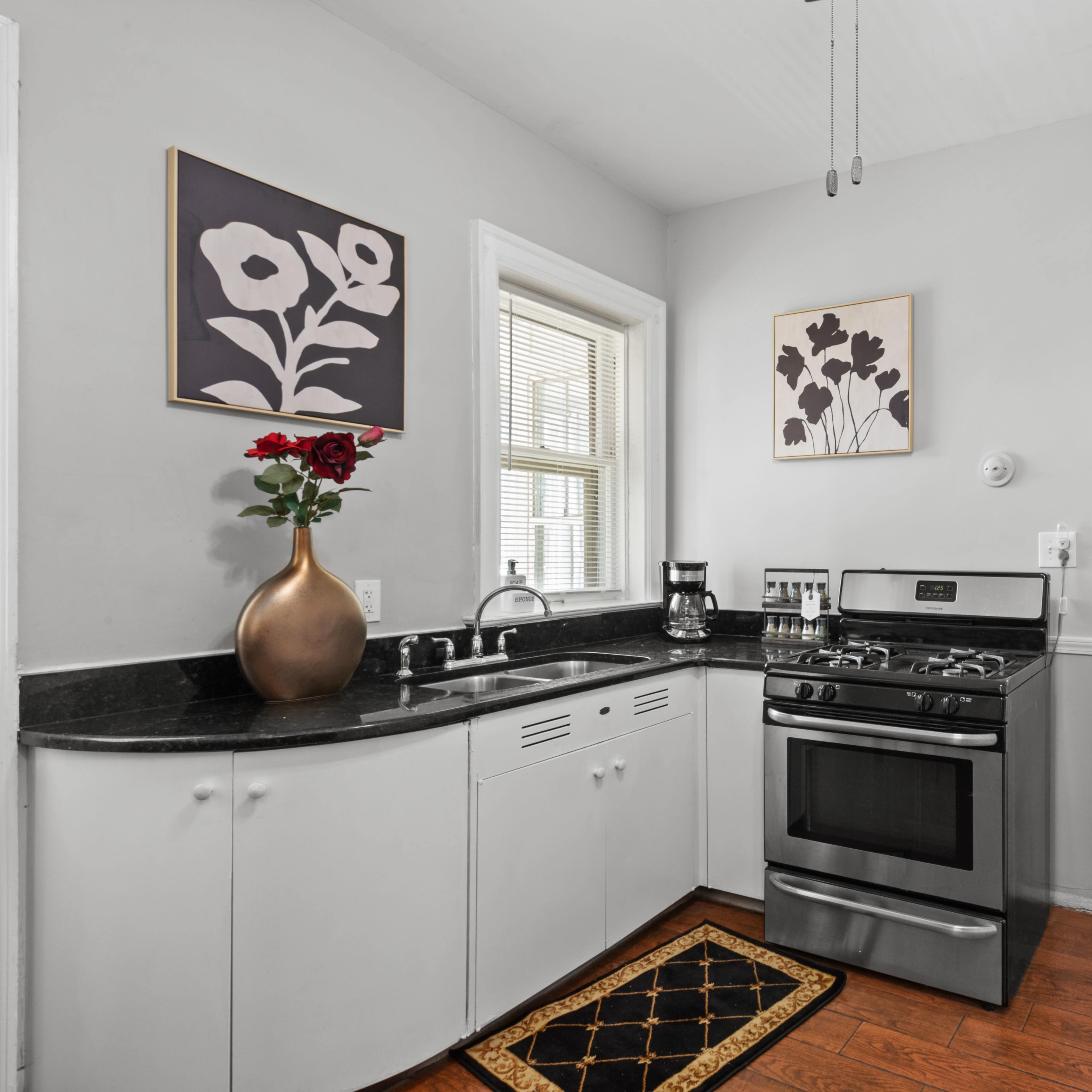 A small kitchen features a gas stove, a black countertop, and framed floral art on the walls.