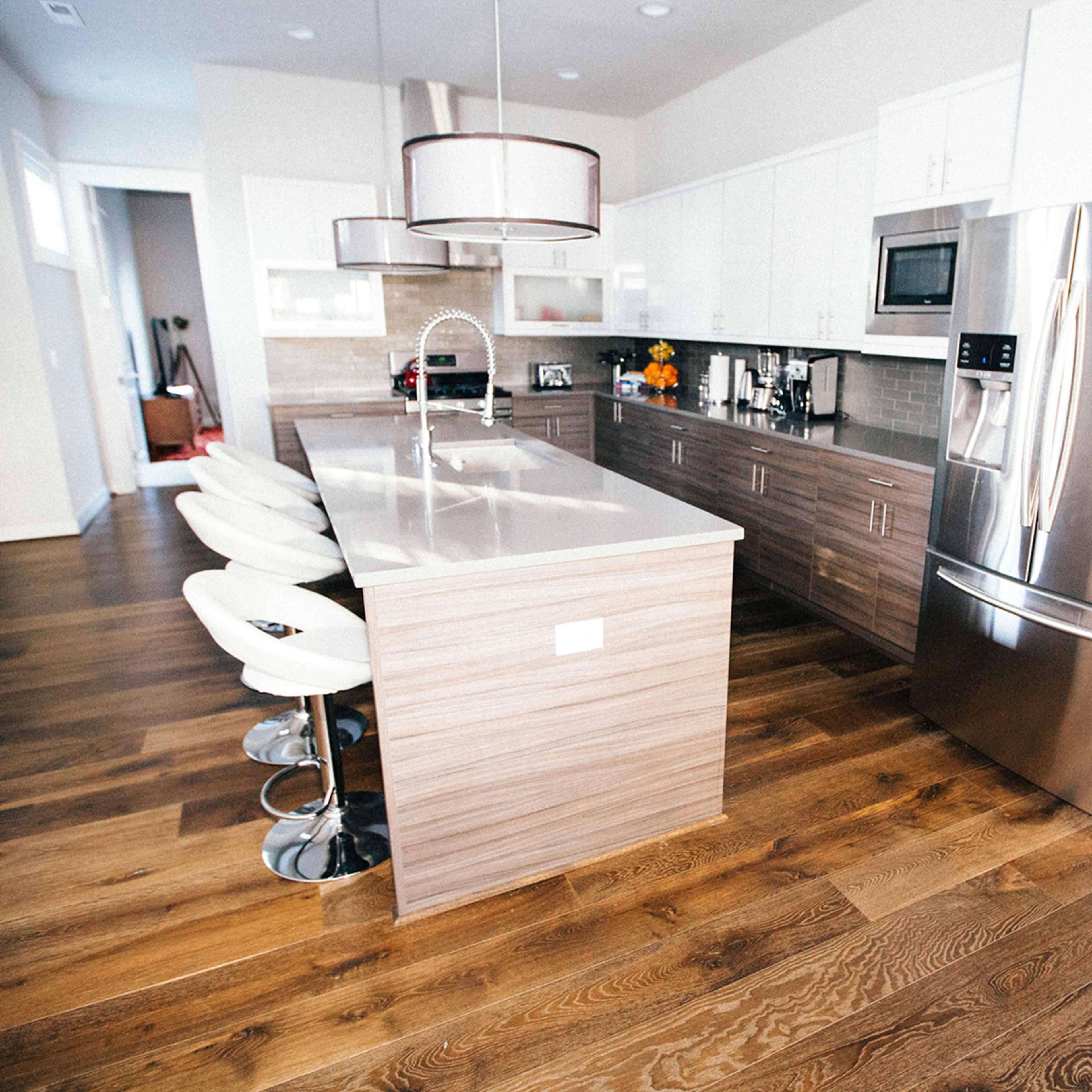 A modern kitchen with a large island featuring bar stools, stainless steel appliances, and light-colored cabinetry.