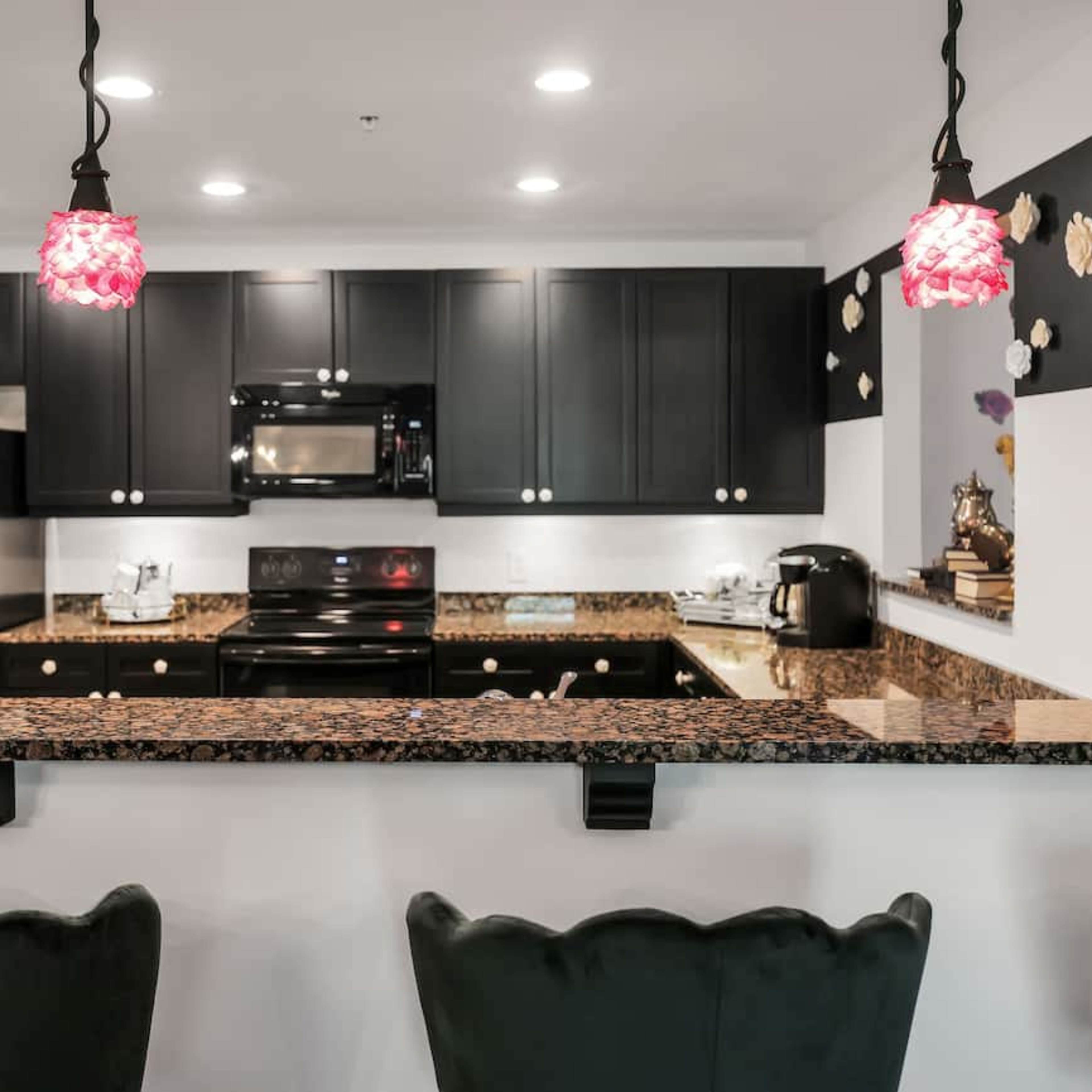 A modern kitchen with dark cabinetry, granite countertops, and pendant lighting above a breakfast bar.
