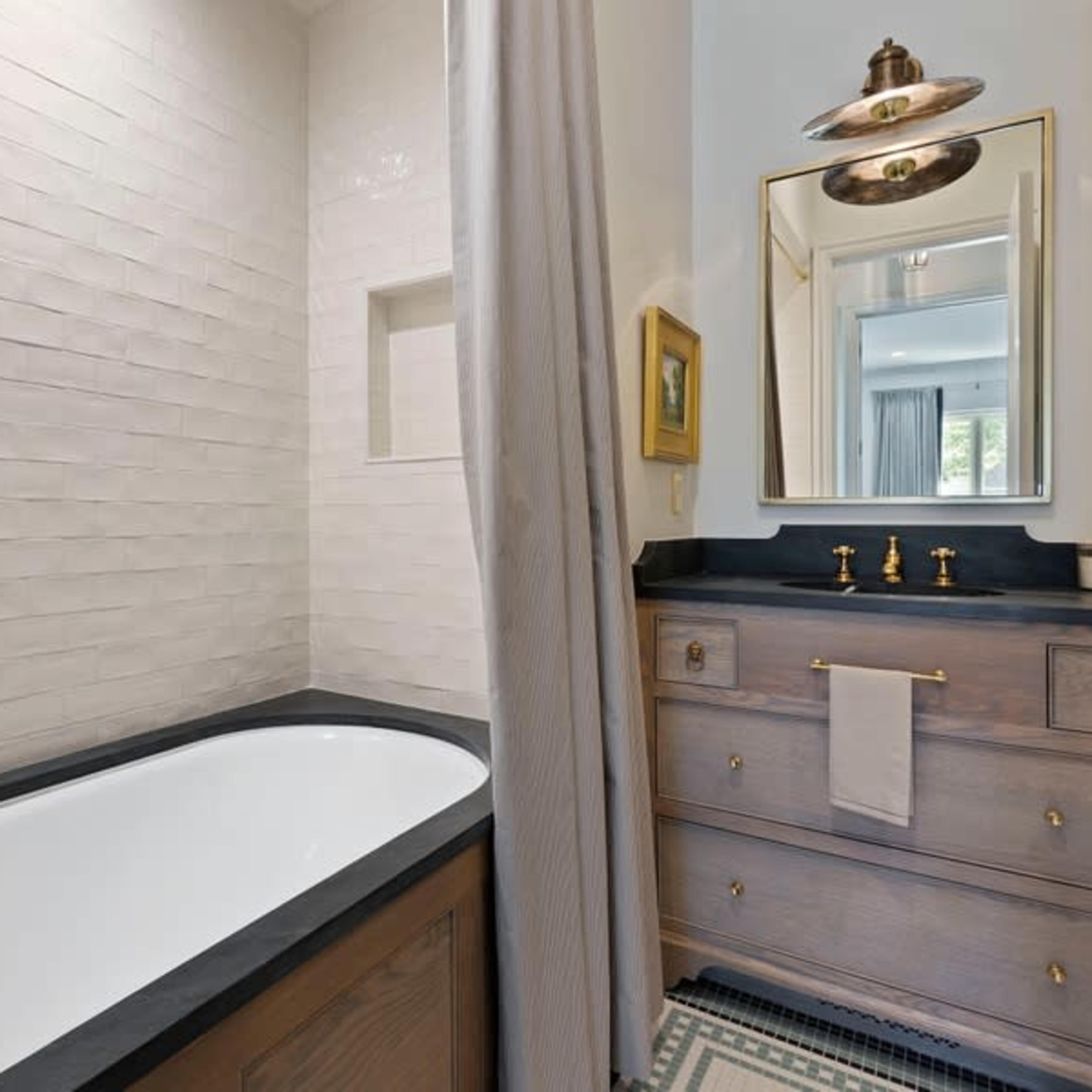 A modern bathroom featuring a freestanding bathtub, a wall-mounted mirror, and a dresser with brass fixtures.