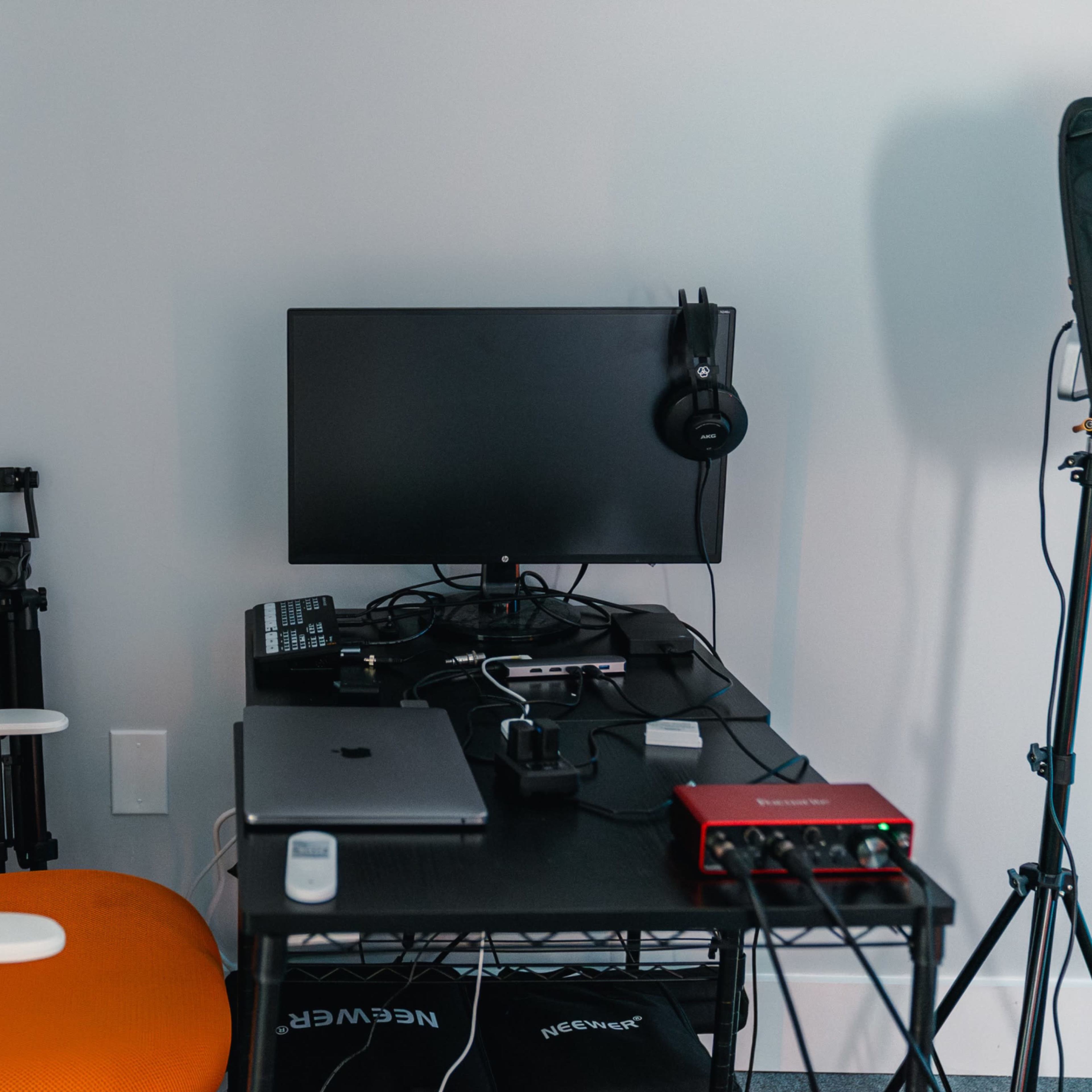 A workspace setup features an orange chair, a computer monitor, audio equipment, and camera tripods in a corner.