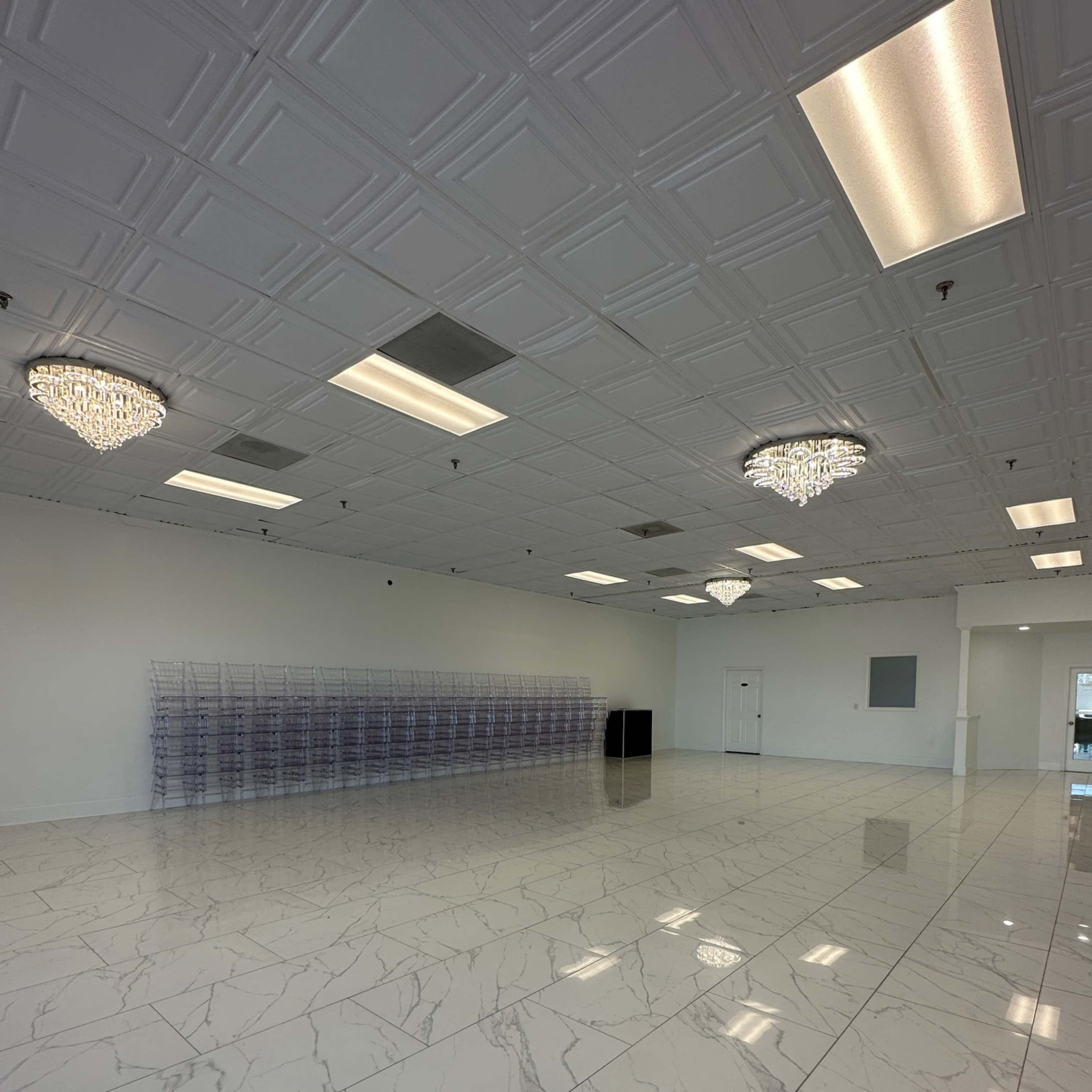 A large, empty commercial space with white marble flooring, ceiling lights, and two crystal chandeliers.