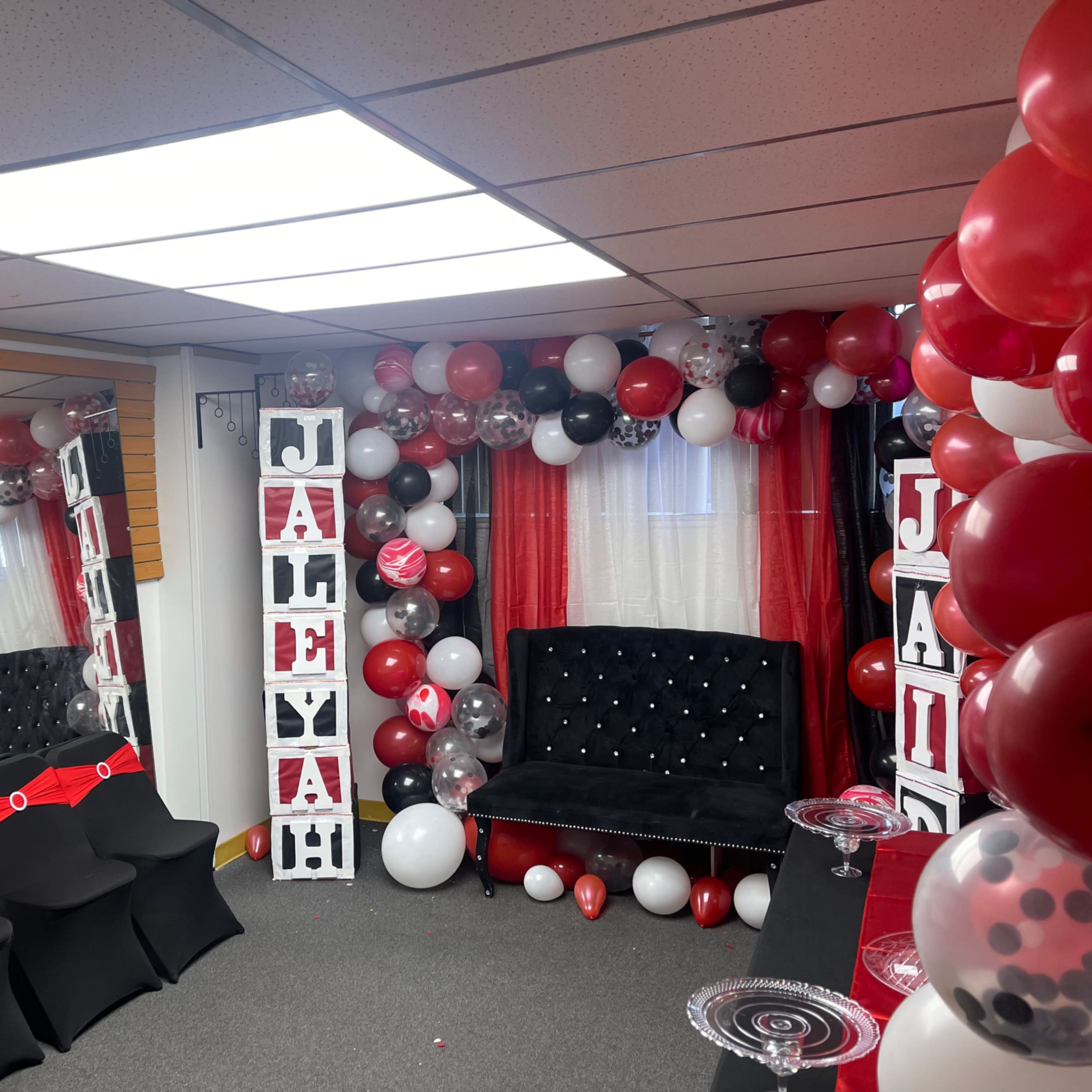 A decorated room with black and red balloons, a black couch, and a display of balloons and letters spelling "JALELYAH."