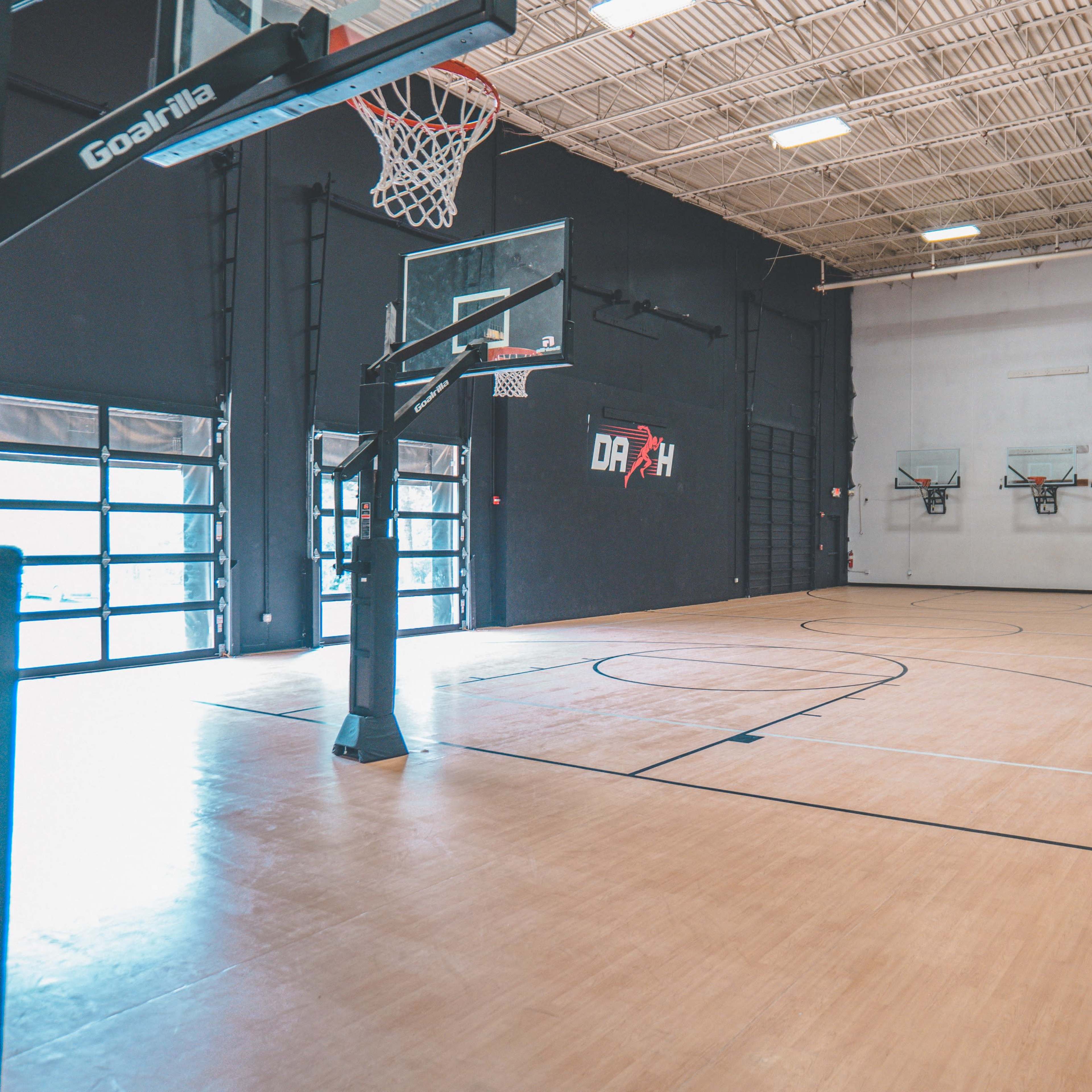 An empty indoor basketball court with three basketball hoops and a black exterior wall.