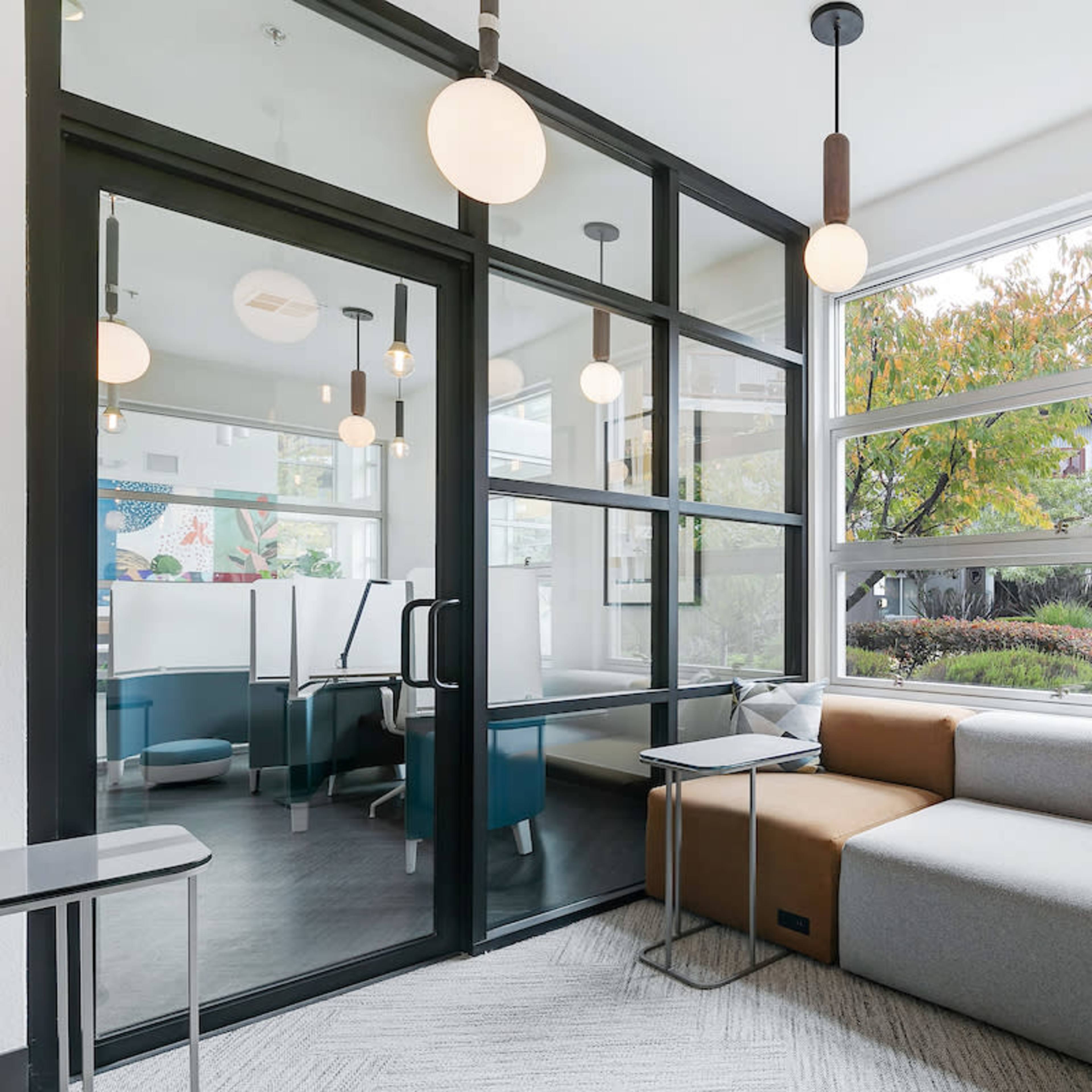 A modern lounge area with a sectional sofa, large windows, and a glass partition separating it from another room.
