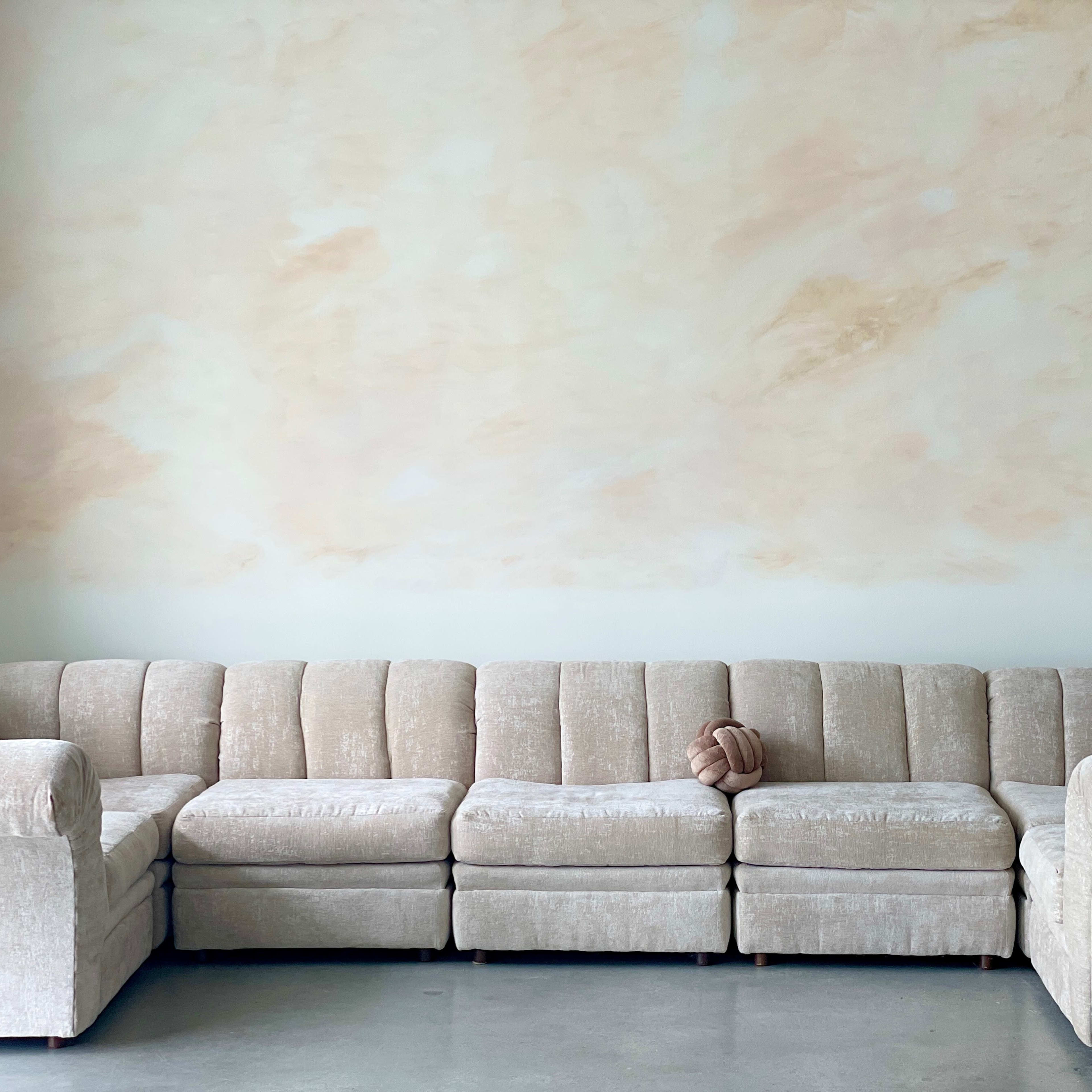 A light-colored sectional sofa is positioned against a softly painted beige wall in a minimalist setting.