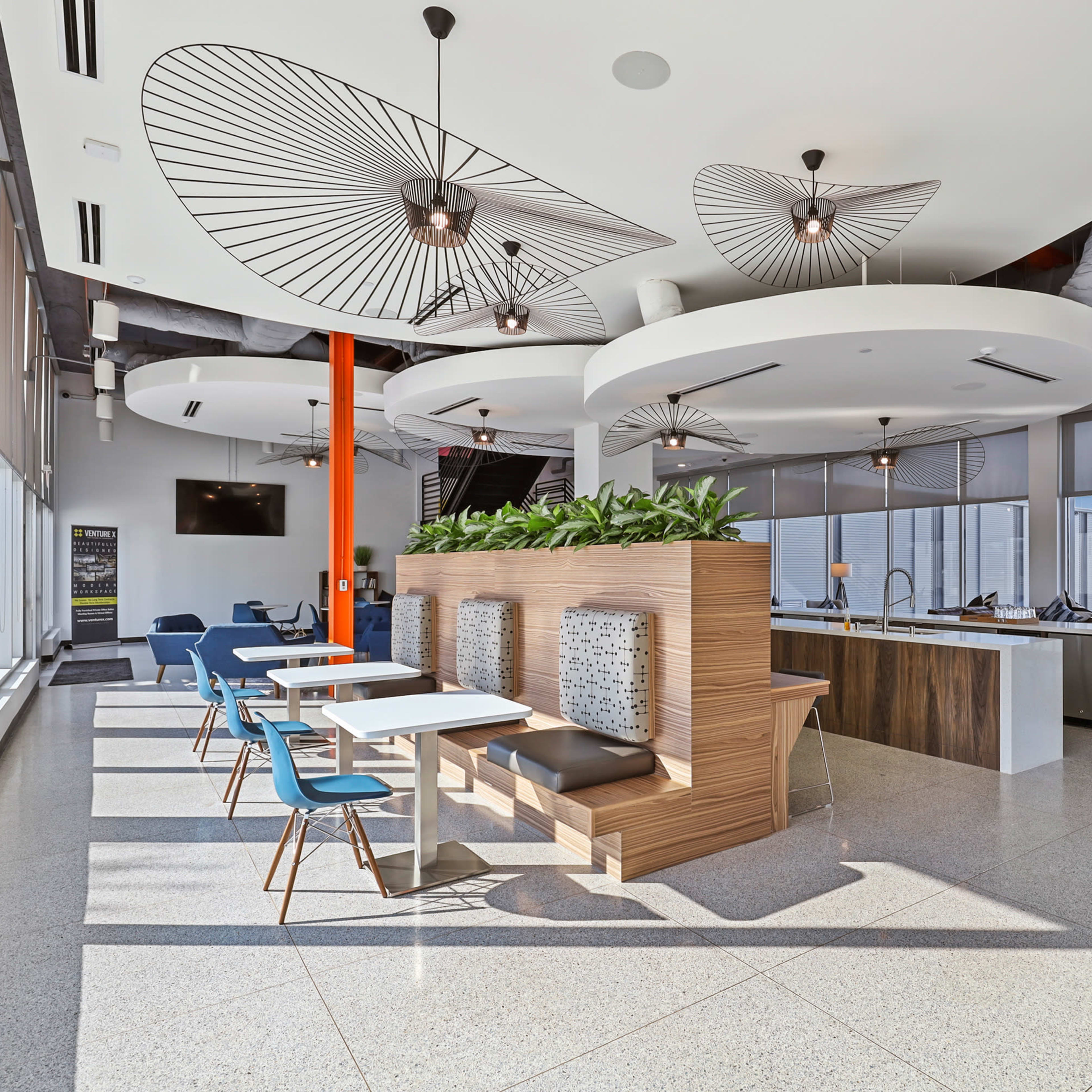 A modern interior of an office space featuring a seating area with booths, a reception desk, and large windows allowing natural light to fill the room.