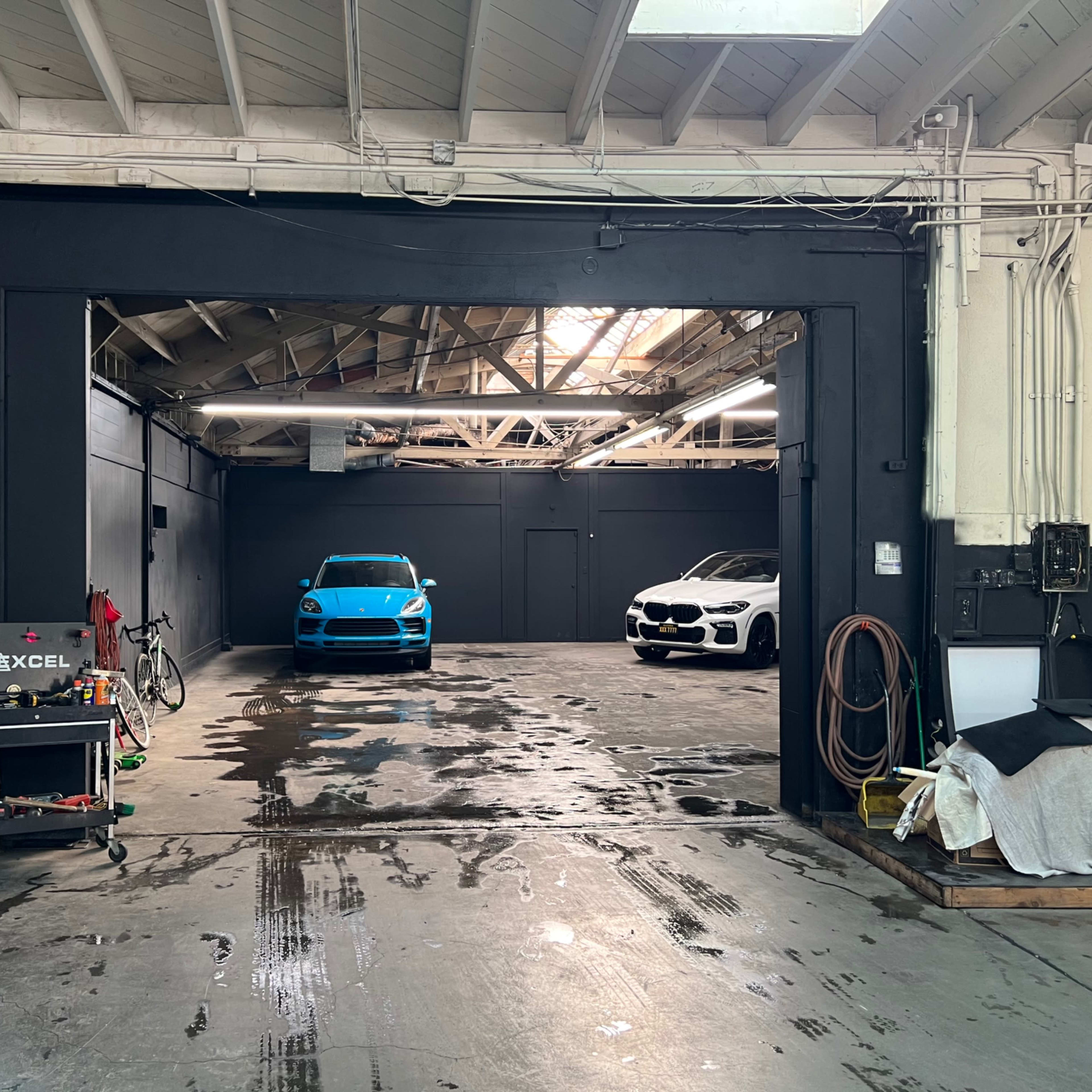 A blue sports car and a white sedan are parked in a spacious garage with a polished concrete floor.