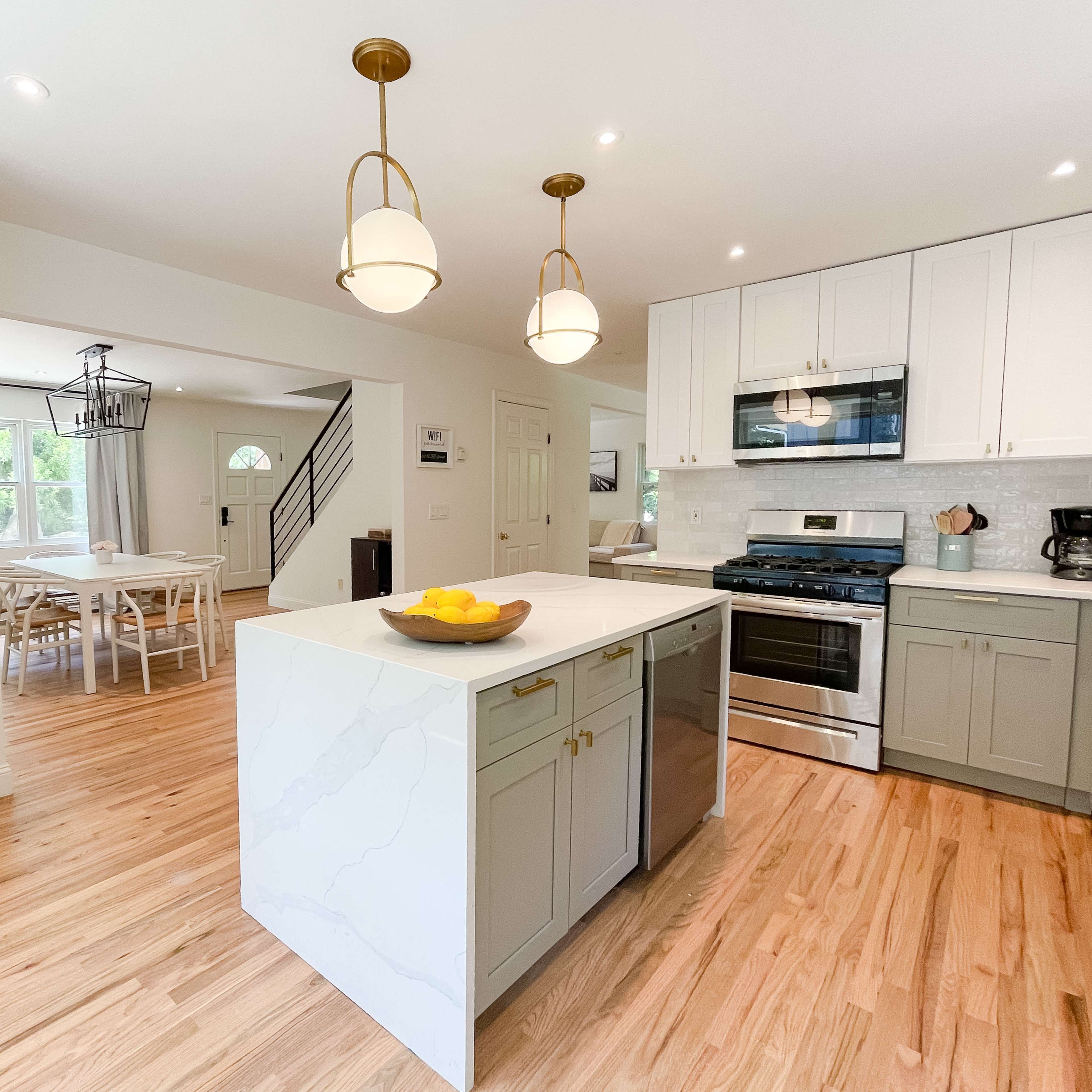 A bright kitchen with an island that has a bowl of lemons, modern appliances, and white cabinetry.