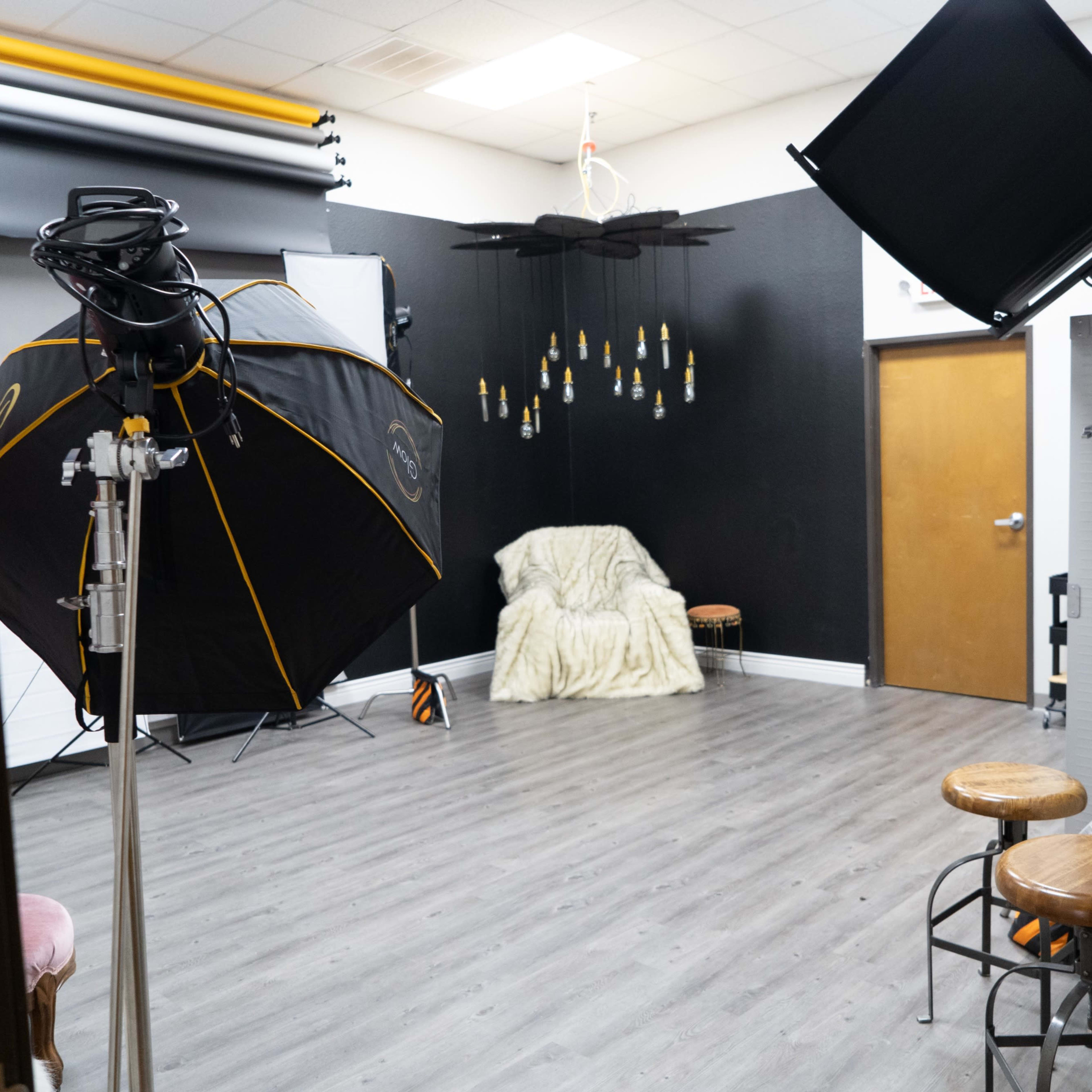 A photography studio with lighting equipment, a draped chair, and a black backdrop.