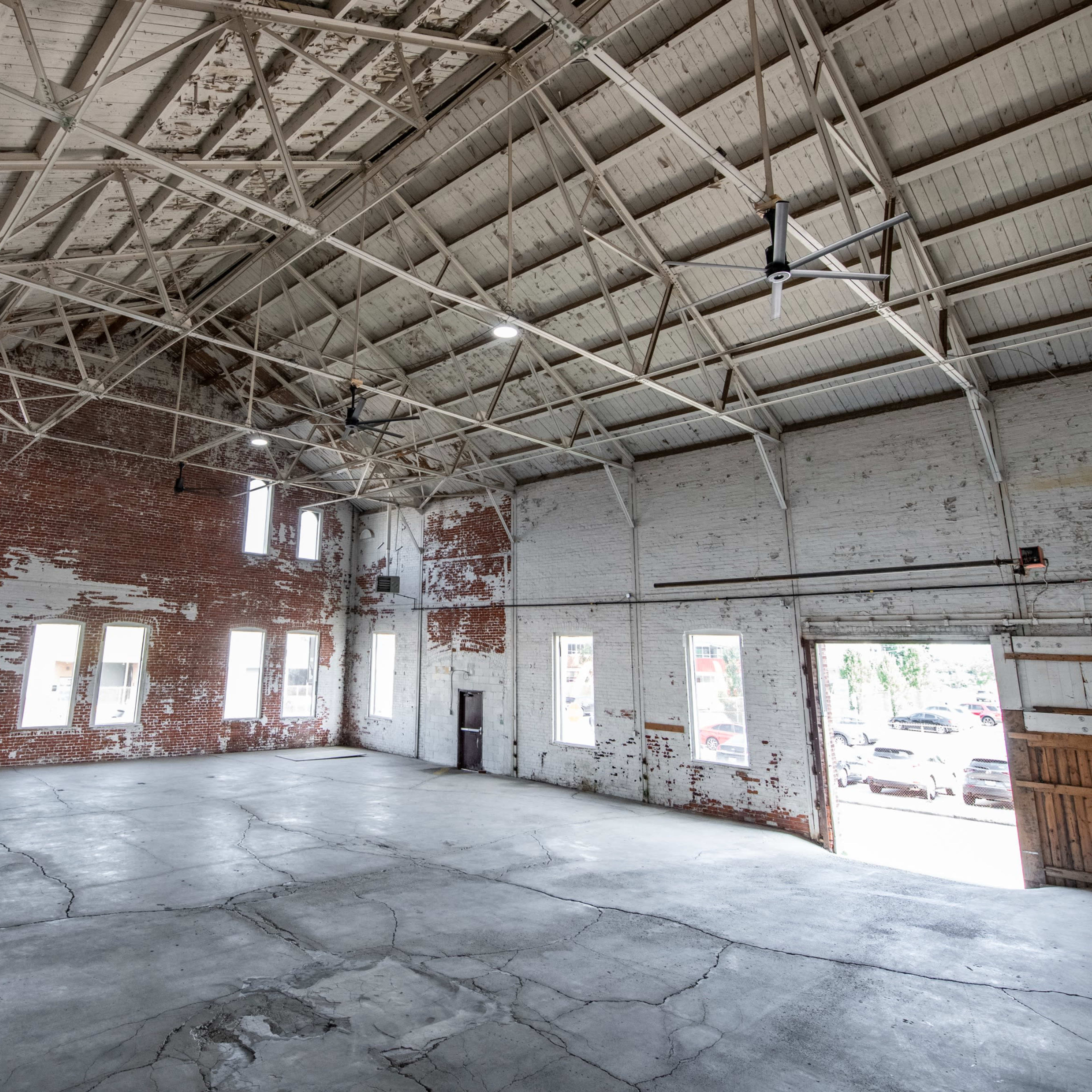 A spacious, empty industrial warehouse with exposed brick walls and a high ceiling.