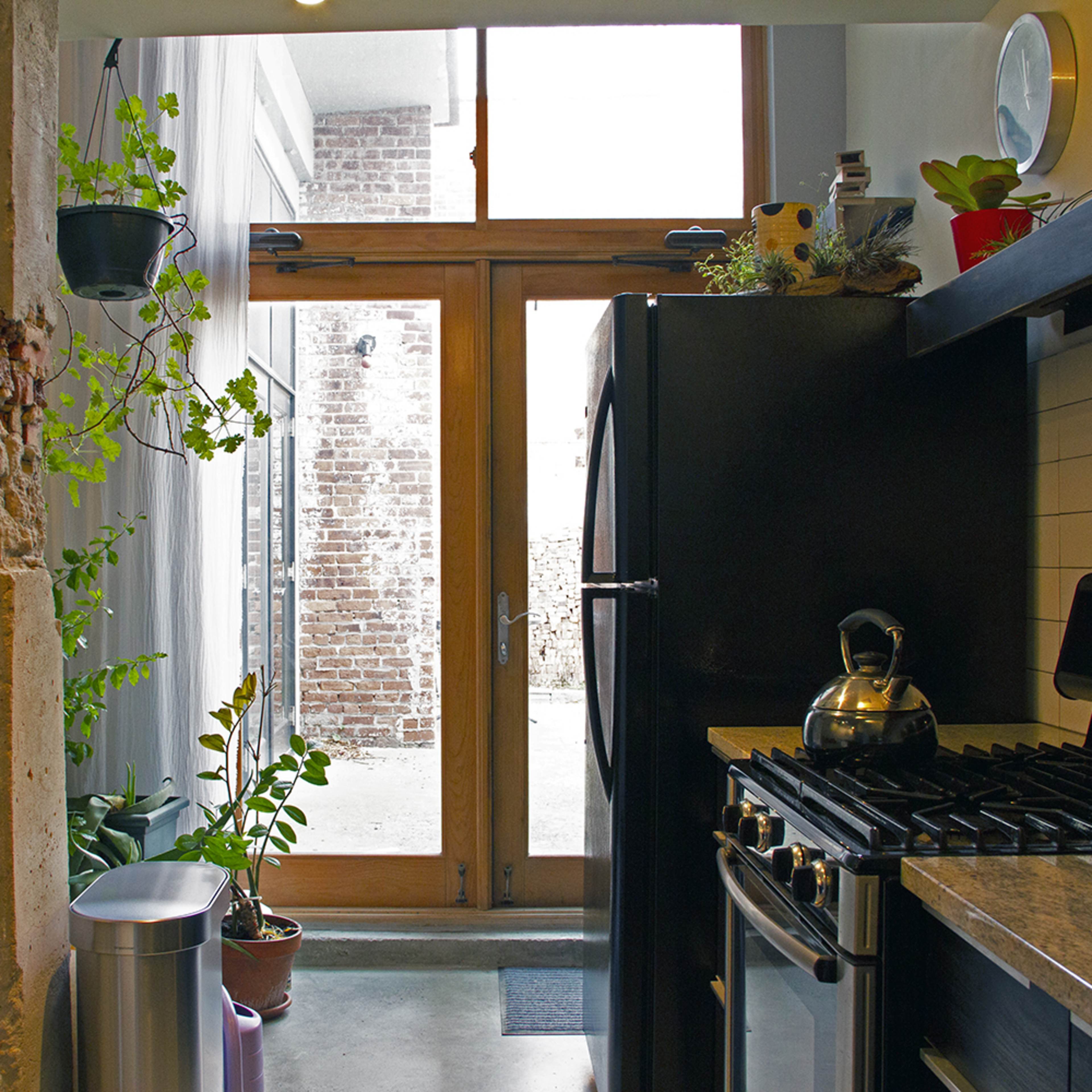 A modern kitchen with a view of an interior courtyard through large glass doors framed by exposed brick and plants.