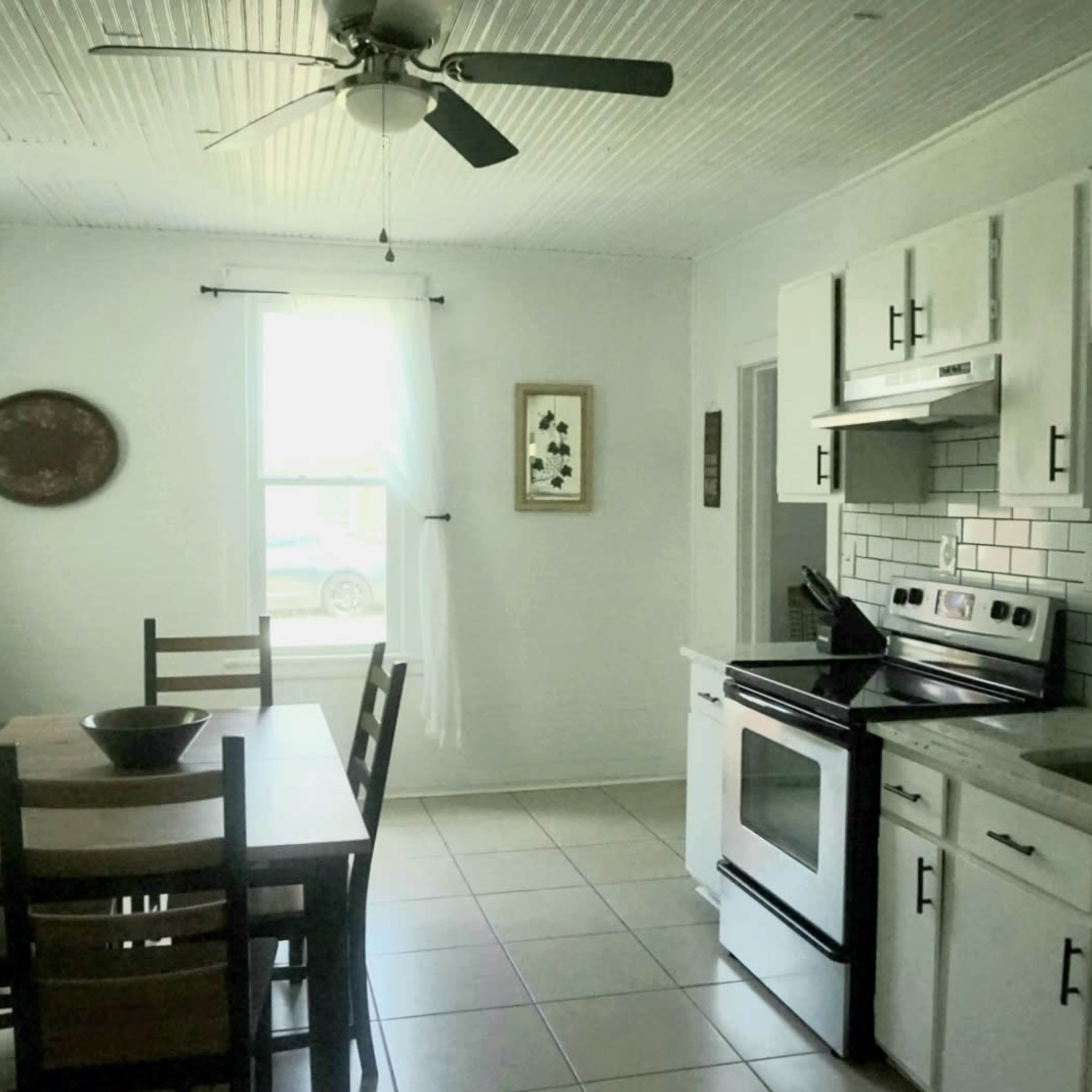 A bright kitchen with a dining table, white cabinetry, a stove, and a window letting in natural light.