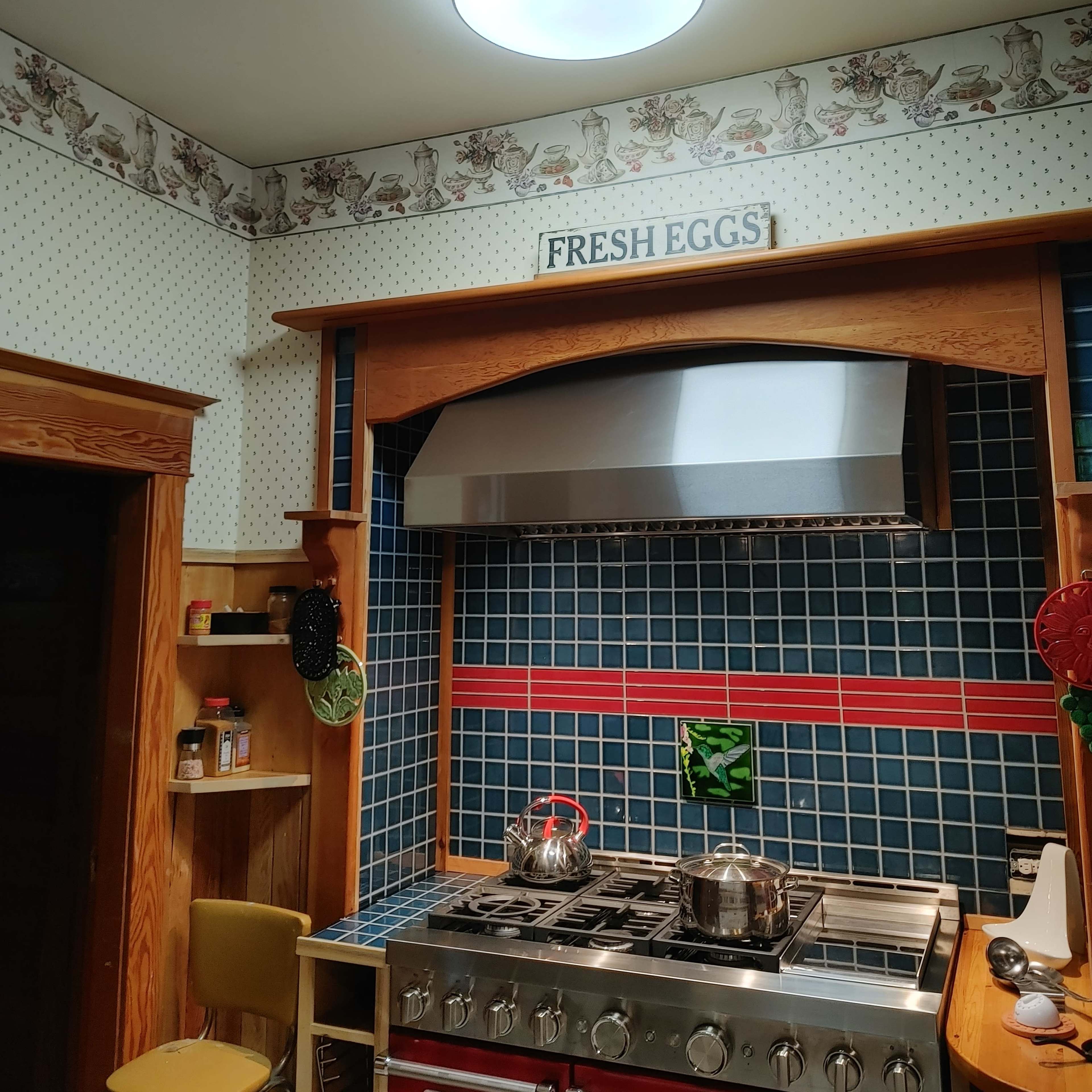 A kitchen with a stainless steel stove, dark blue tiled backsplash, and a decorative sign reading "FRESH EGGS" above the countertop.