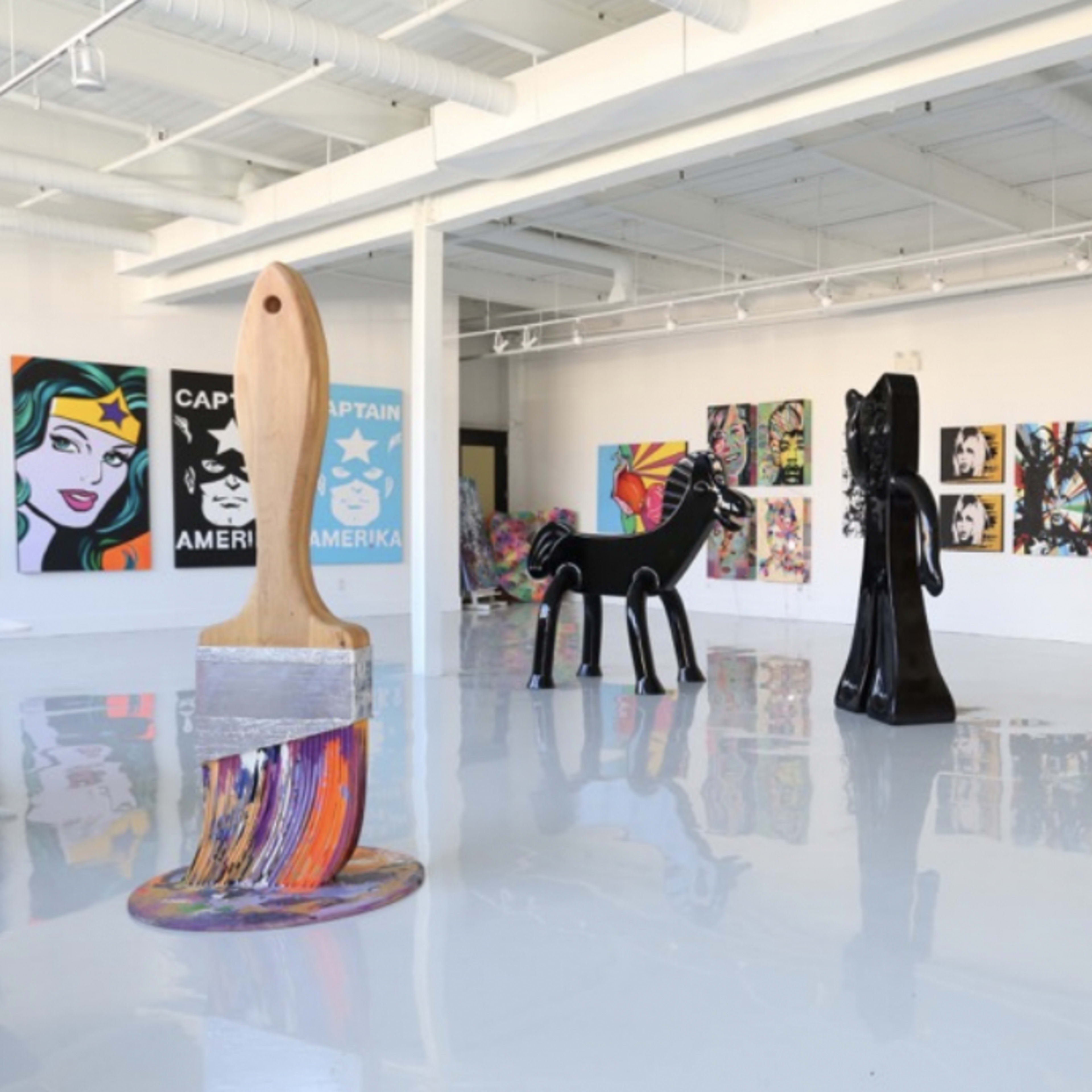 An art gallery featuring colorful paintings on the walls and large sculptural pieces, including a paintbrush and a horse.