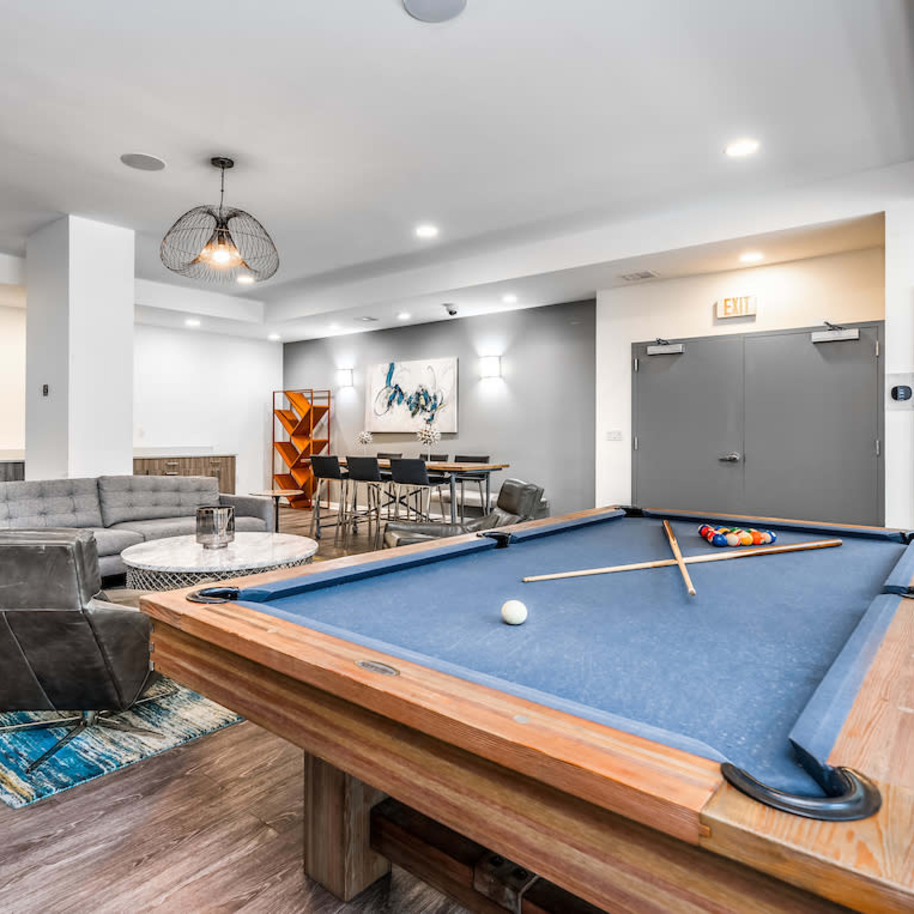 A modern game room featuring a pool table, a circular dining table, a sectional sofa, and stylish lighting fixtures.