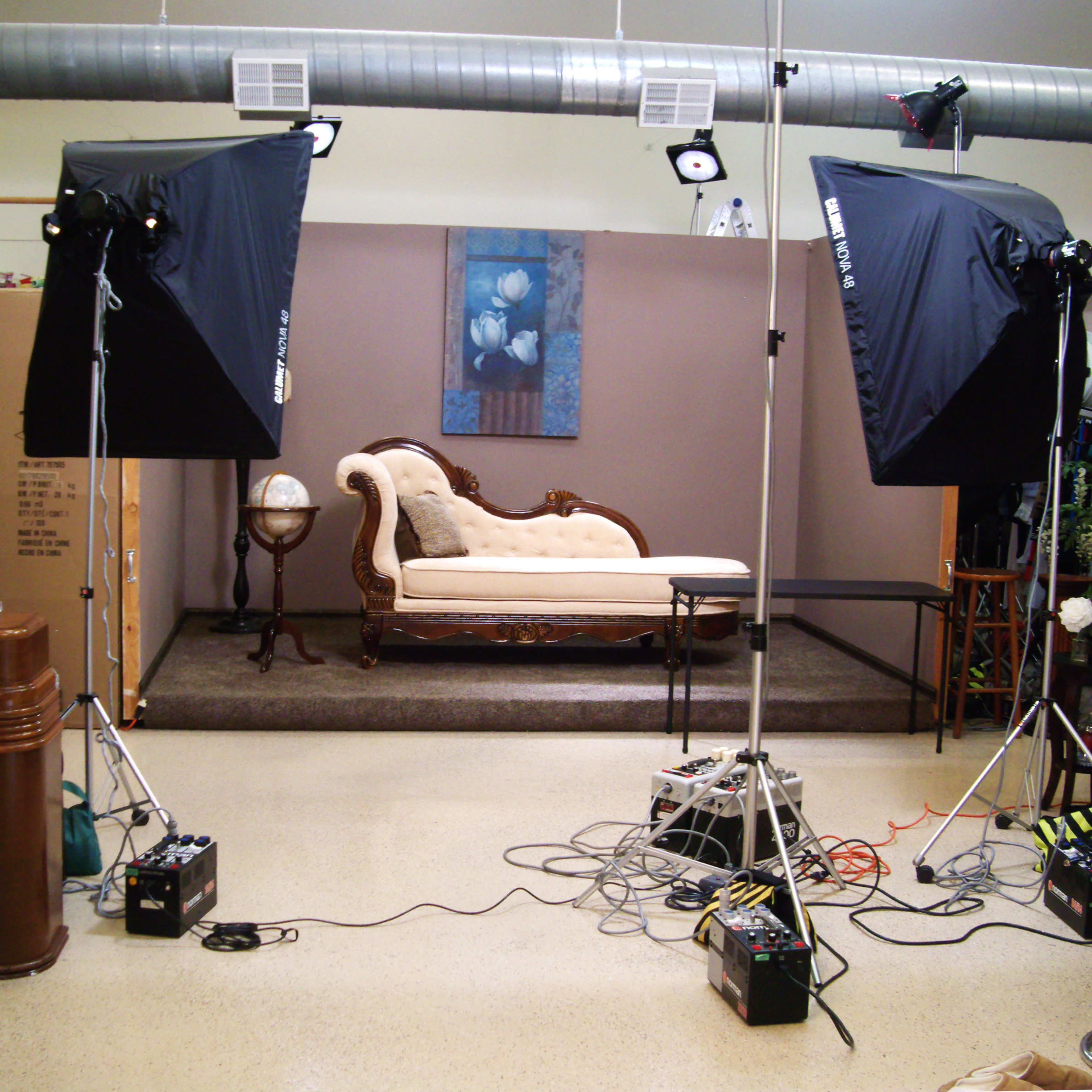 A photography studio set up with two large softbox lights, a vintage sofa, and various electrical equipment on the floor.