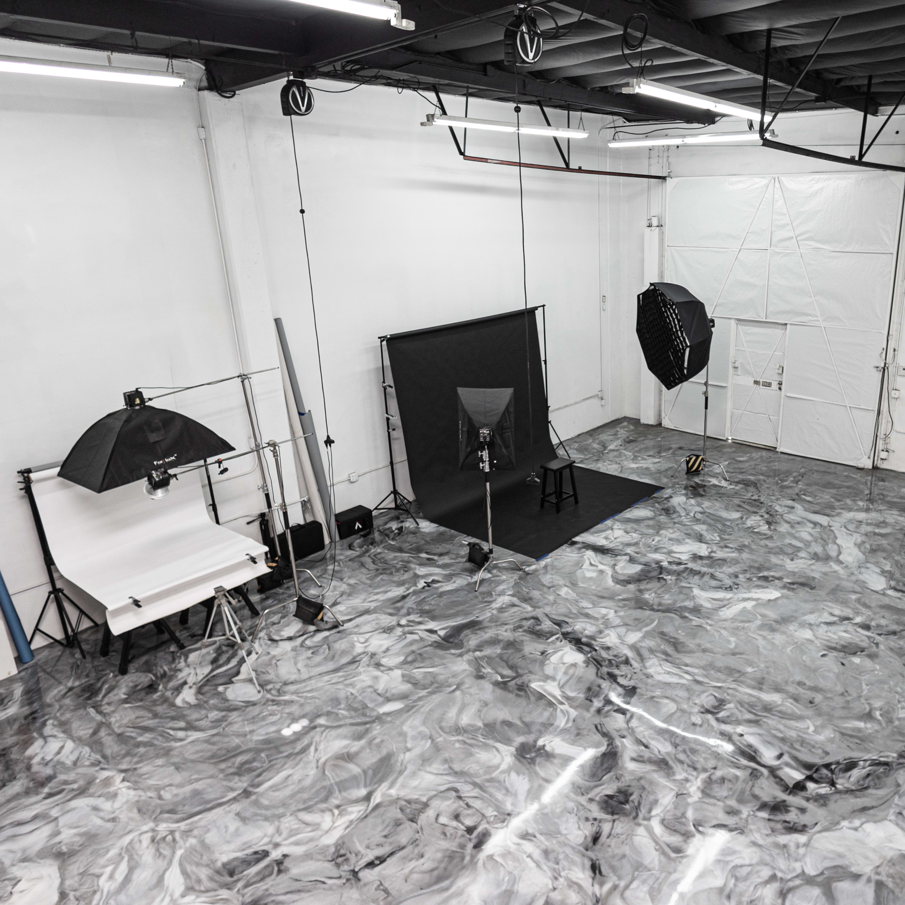 A photography studio features a marbled floor, a black backdrop with a chair, and lighting equipment set up for a shoot.