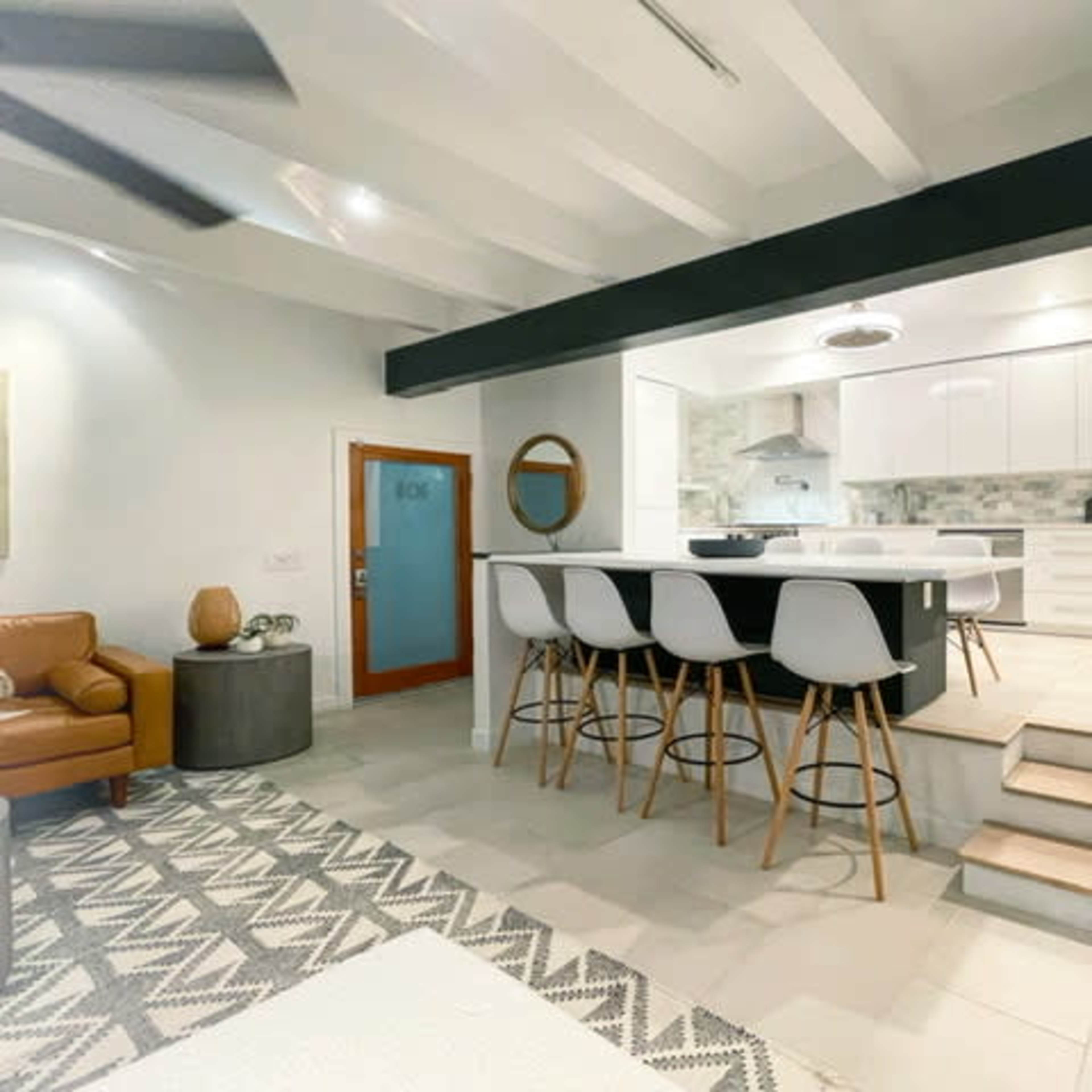 A modern living space featuring a kitchen and dining area with white cabinetry, bar stools, and a cozy seating area with a brown leather chair.